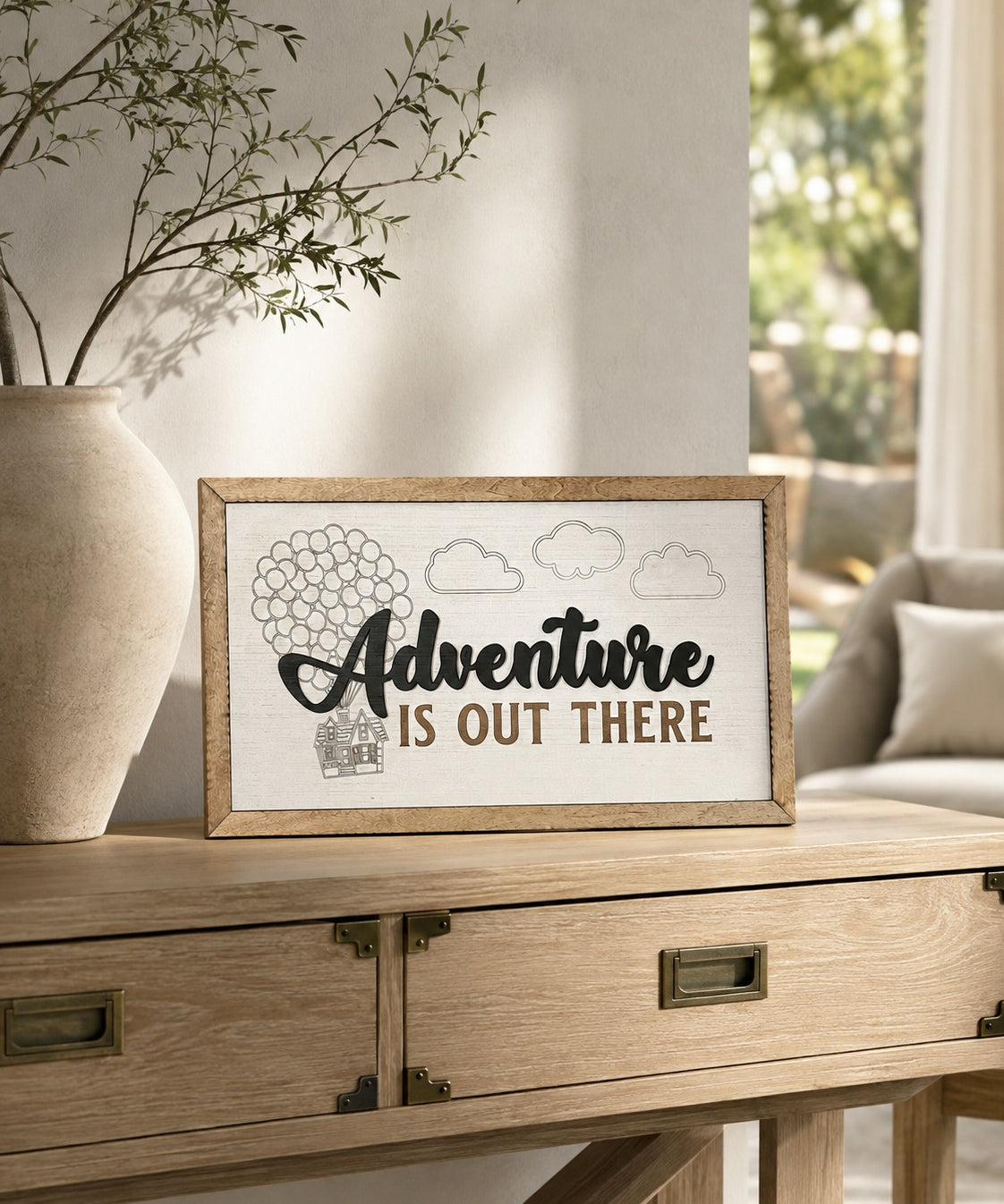 Adventure Is Out There balloon house framed wood sign styled on a light oak console in a sunlit conservatory