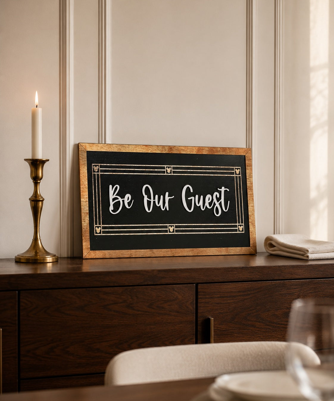 Be Our Guest black framed wood sign with script lettering styled on a walnut dresser