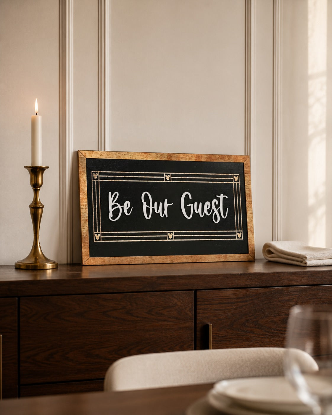 Be Our Guest black framed wood sign with script lettering styled on a walnut dresser
