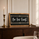 Be Our Guest black framed wood sign with script lettering styled on a walnut dresser
