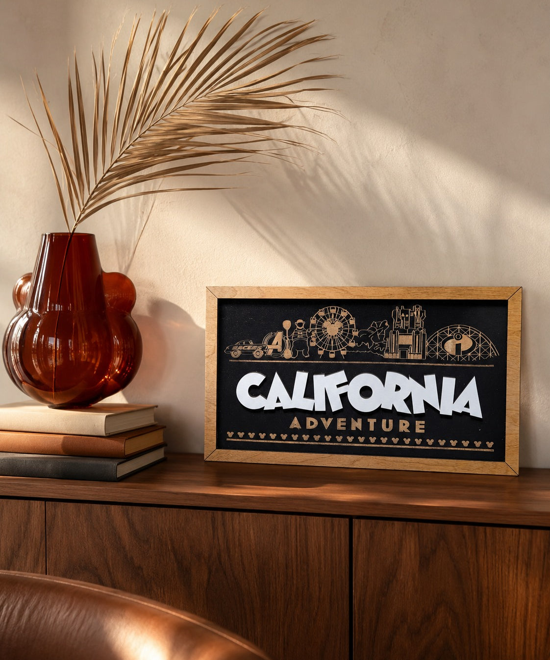 California Adventure skyline framed wood sign styled on a walnut credenza with a dried palm frond