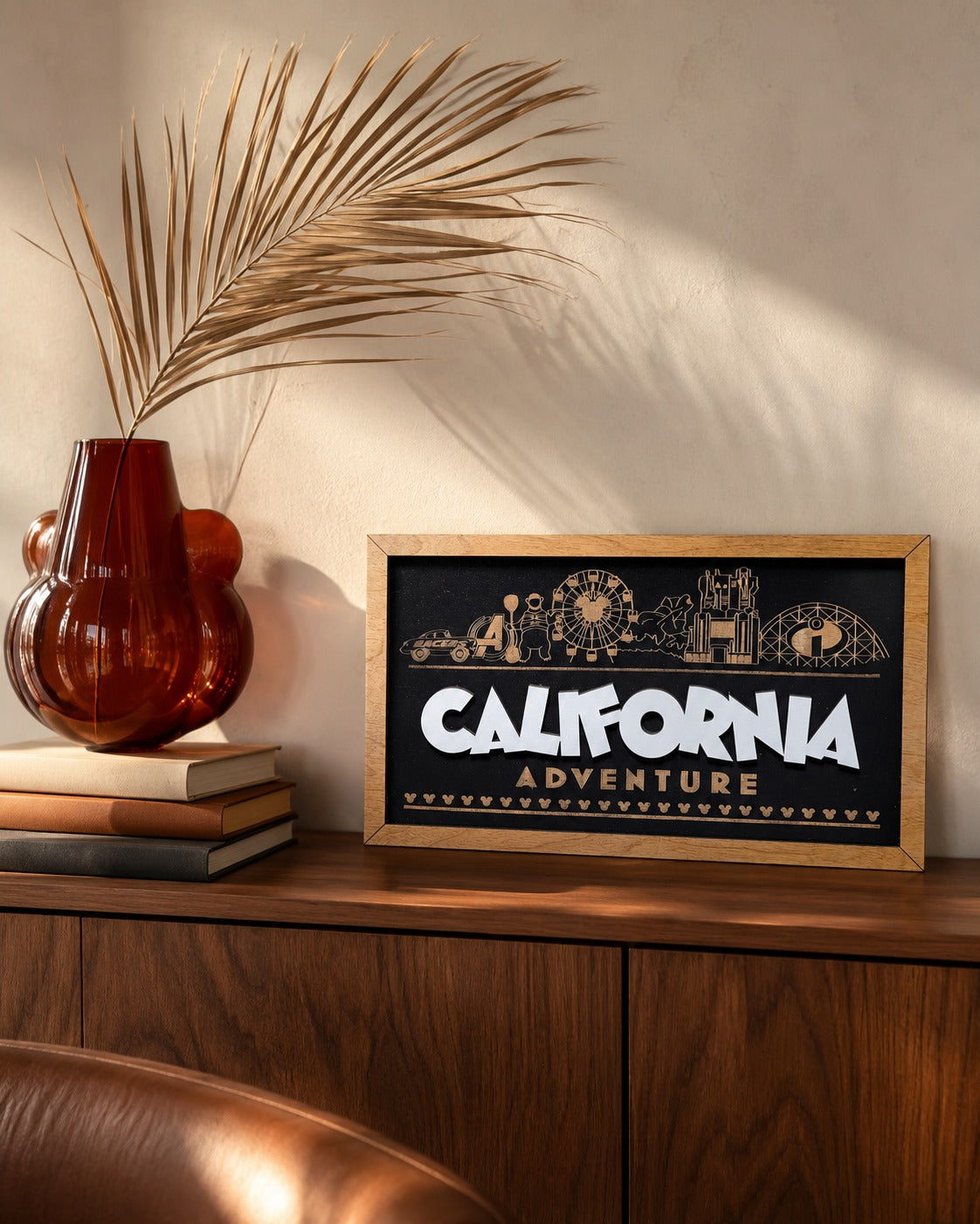 California Adventure skyline framed wood sign styled on a walnut credenza with a dried palm frond