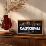 California Adventure skyline framed wood sign styled on a walnut credenza with a dried palm frond