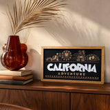 California Adventure skyline framed wood sign styled on a walnut credenza with a dried palm frond