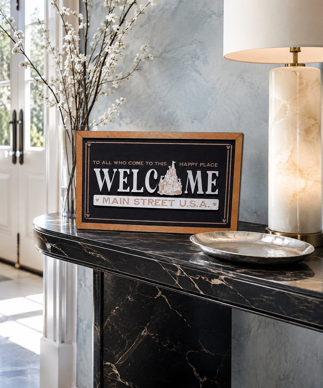 Welcome Main Street USA castle icon framed wood sign styled on a marble console in a luxury foyer