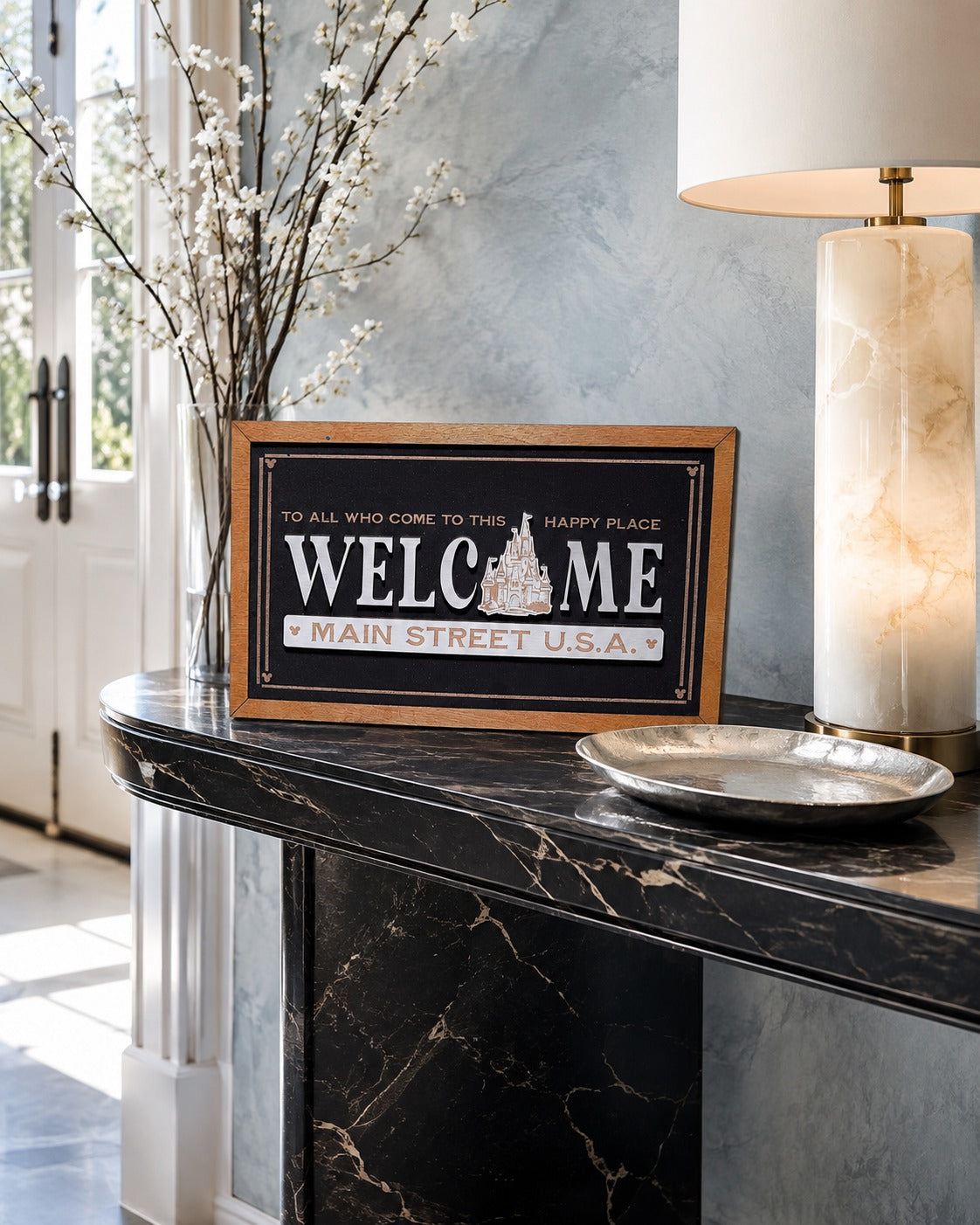 Welcome Main Street USA castle icon framed wood sign styled on a marble console in a luxury foyer