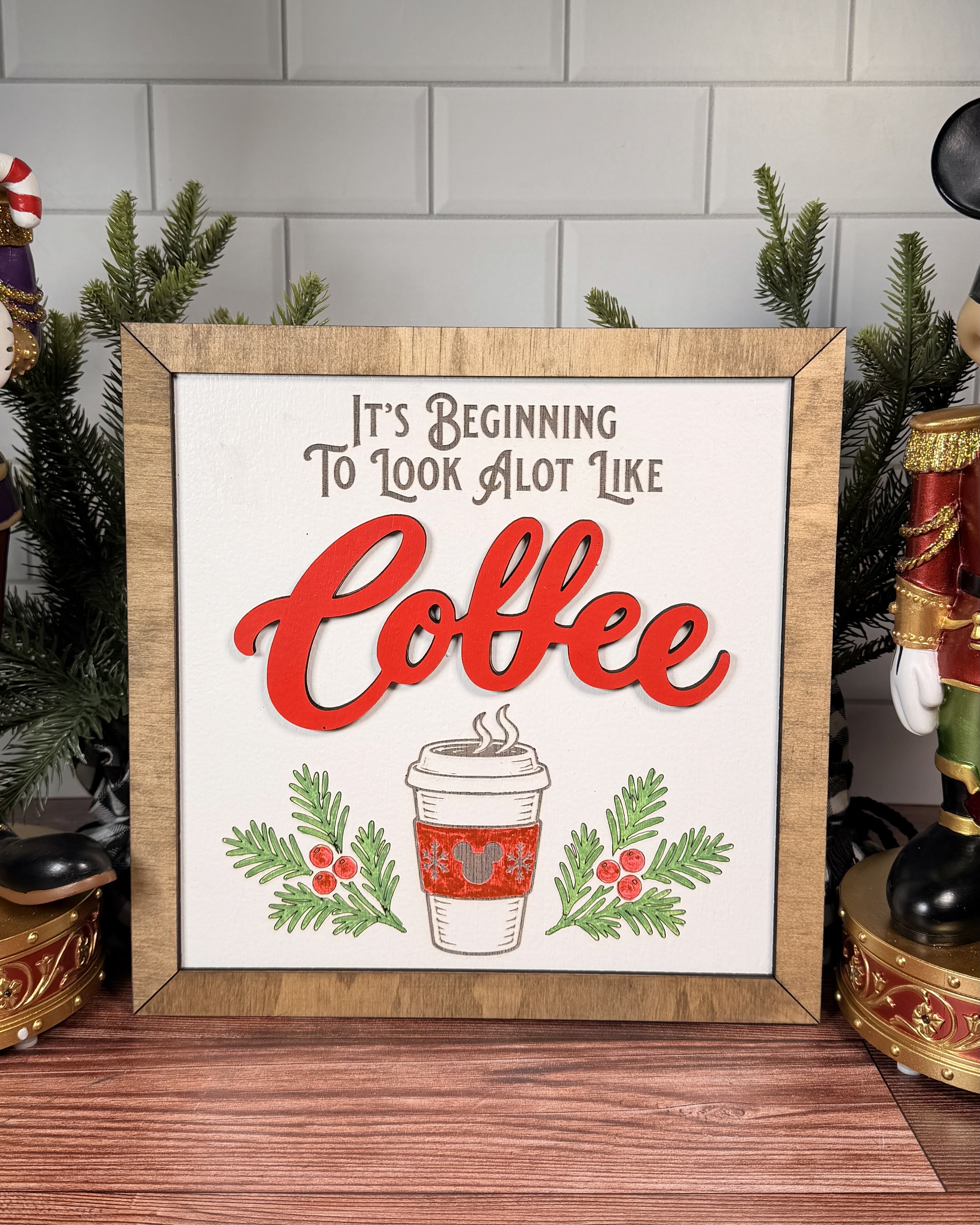 It's Beginning to Look a Lot Like Coffee square Christmas sign with red layered Coffee lettering, a takeaway cup, evergreen sprigs and a brown wood frame.