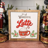 It's a Wonderful Latte square Christmas sign with red layered Latte lettering, a whipped-cream mug and candy cane, evergreen sprigs and a brown wood frame.