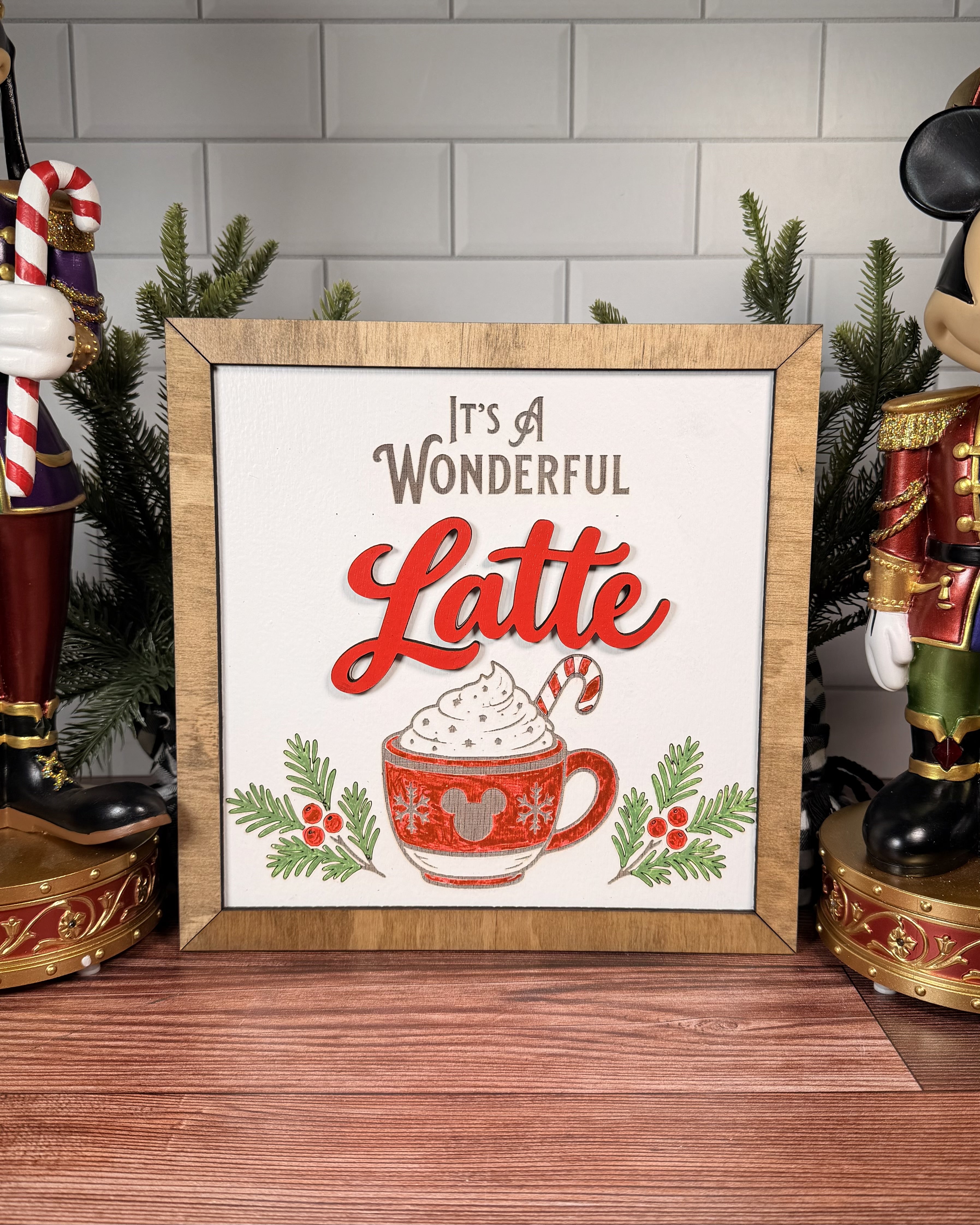 It's a Wonderful Latte square Christmas sign with red layered Latte lettering, a whipped-cream mug and candy cane, evergreen sprigs and a brown wood frame.