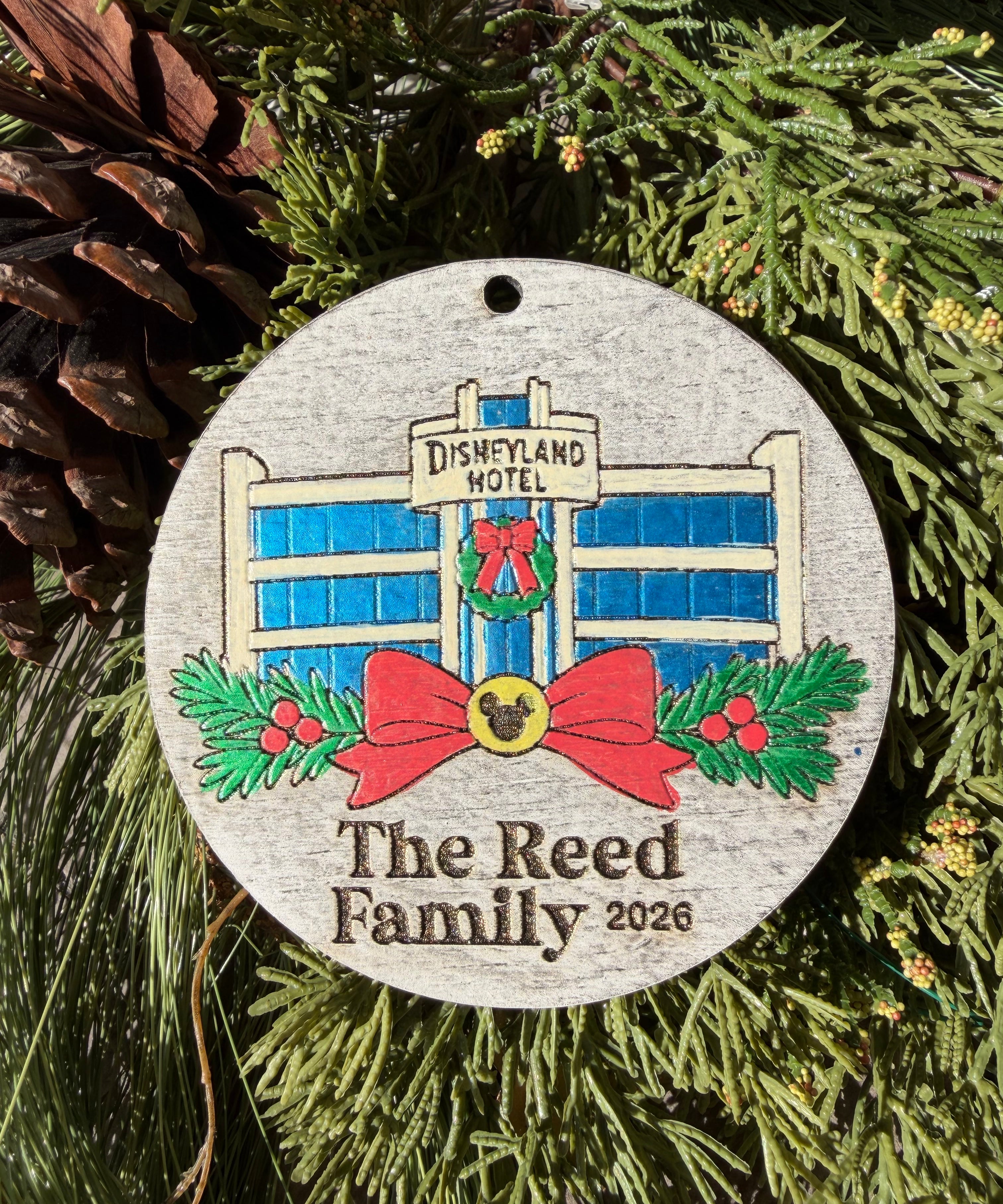 Finished hand-painted Original Park Hotel Christmas Ornament on evergreen greenery. Personal name and year shown are sample personalization.