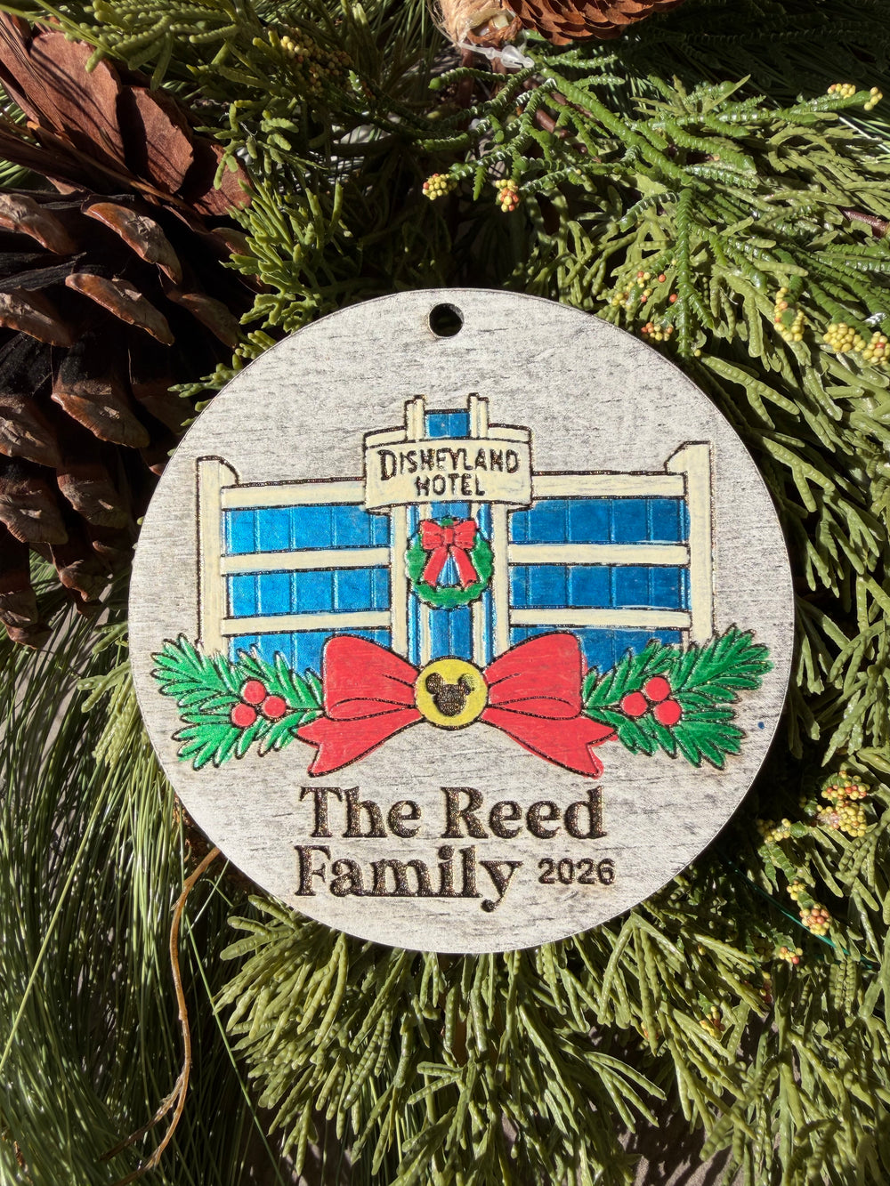 Finished hand-painted Original Park Hotel Christmas Ornament on evergreen greenery. Personal name and year shown are sample personalization.