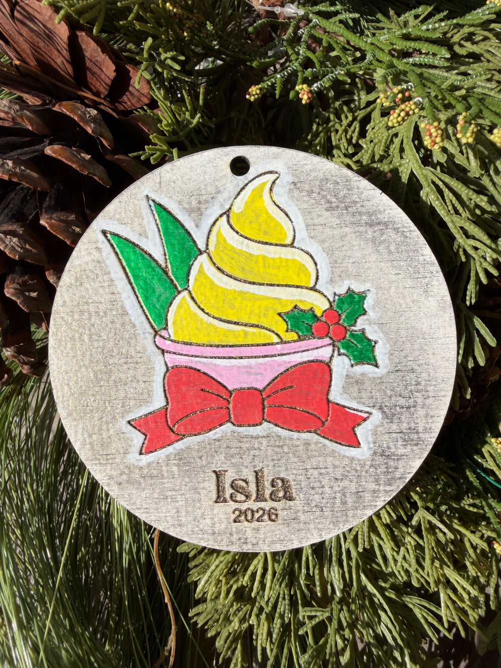Finished hand-painted Pineapple Swirl Christmas Ornament on evergreen greenery. Personal name and year shown are sample personalization.