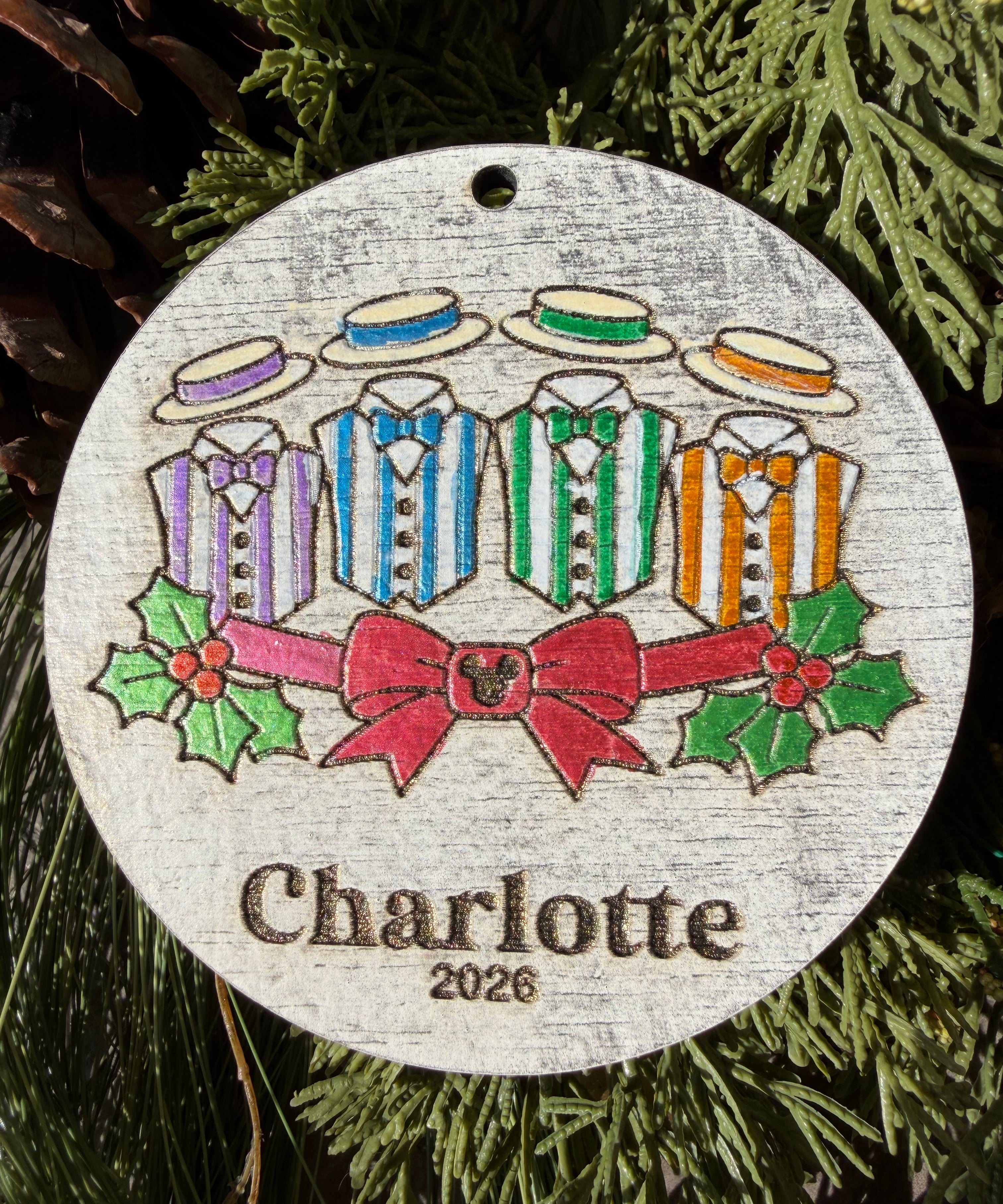 Finished hand-painted Main Street Harmony Christmas Ornament on evergreen greenery. Personal name and year shown are sample personalization.