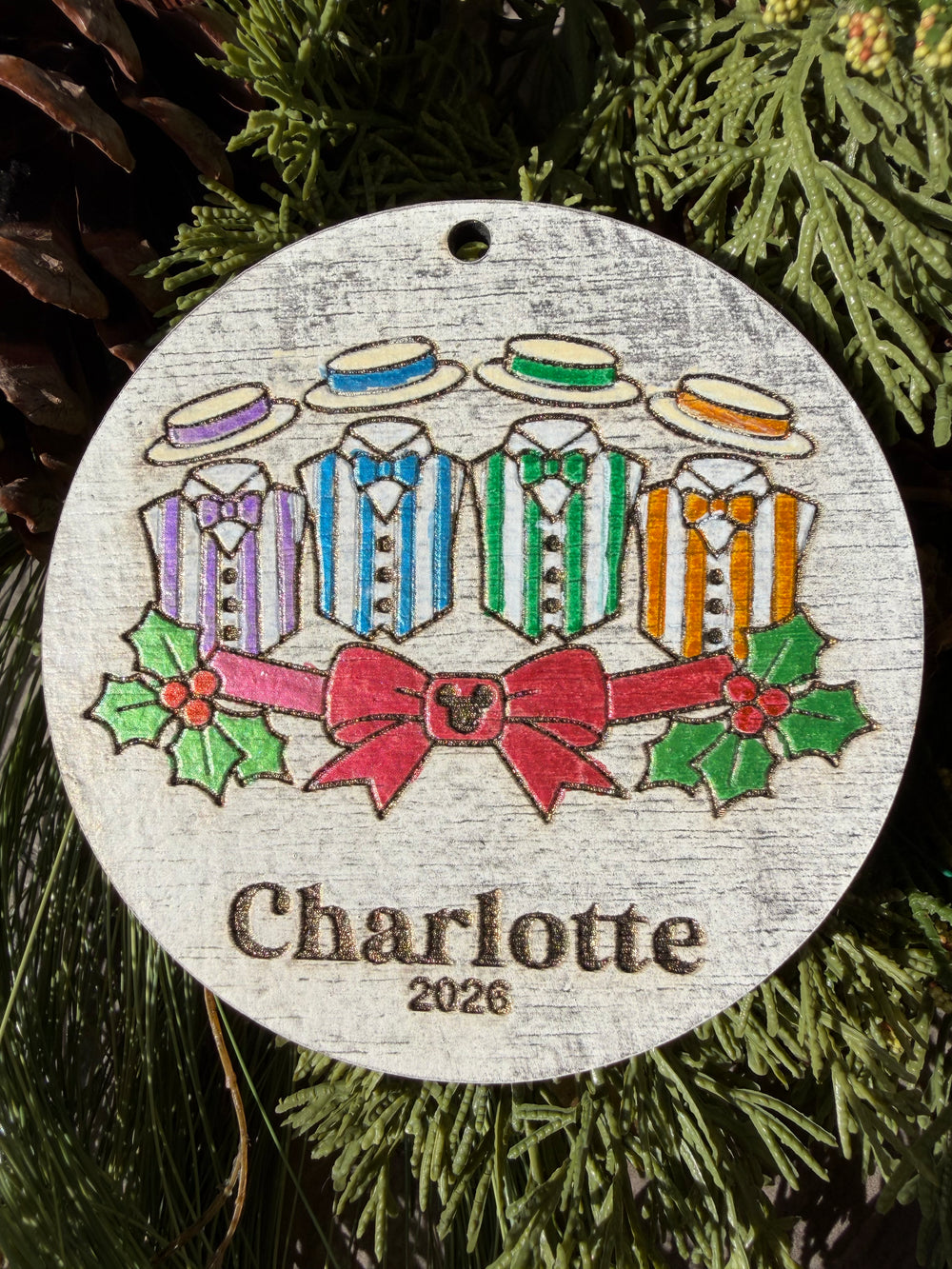 Finished hand-painted Main Street Harmony Christmas Ornament on evergreen greenery. Personal name and year shown are sample personalization.