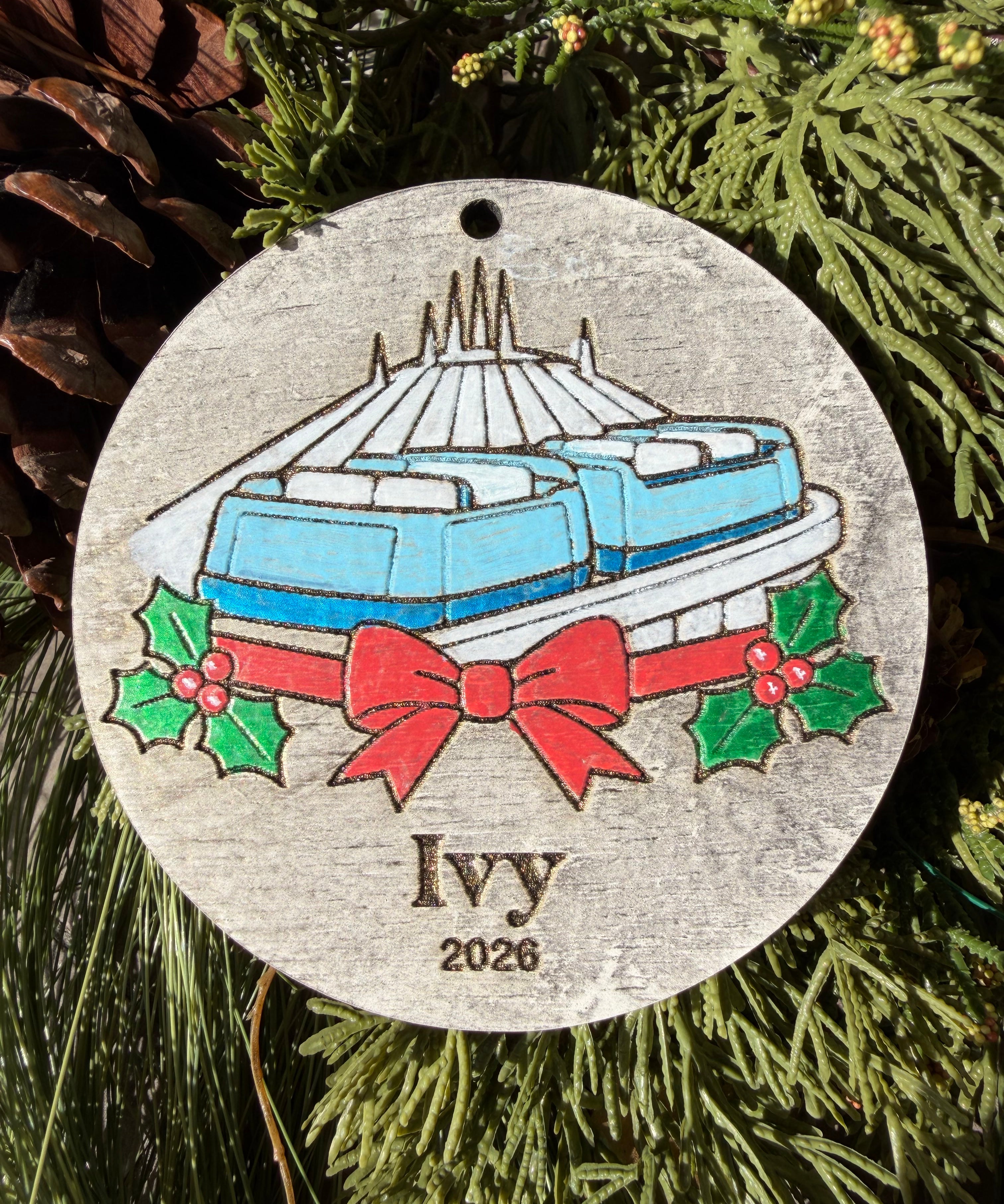 Finished hand-painted PeopleMover Christmas Ornament on evergreen greenery. Personal name and year shown are sample personalization.