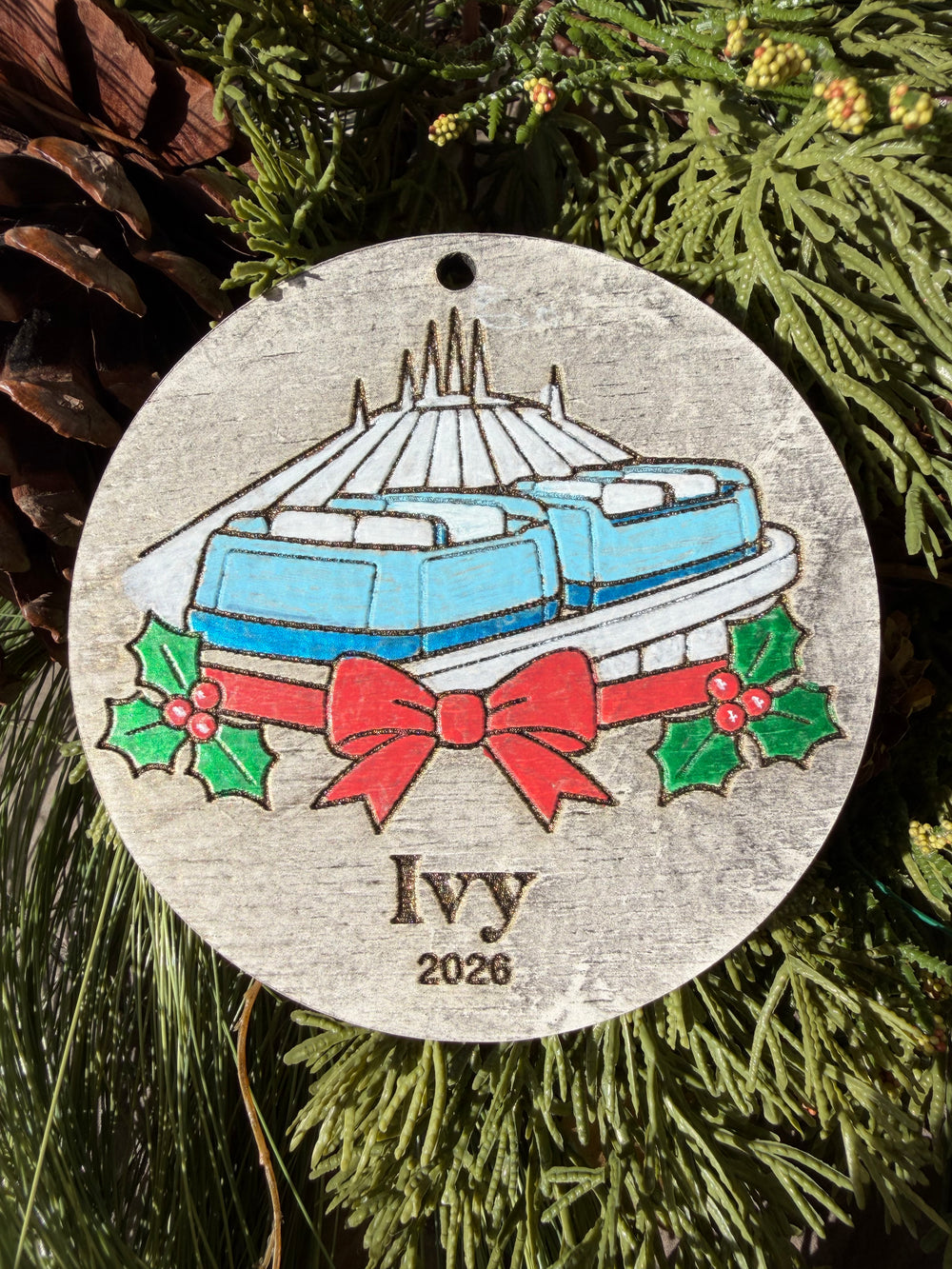 Finished hand-painted PeopleMover Christmas Ornament on evergreen greenery. Personal name and year shown are sample personalization.
