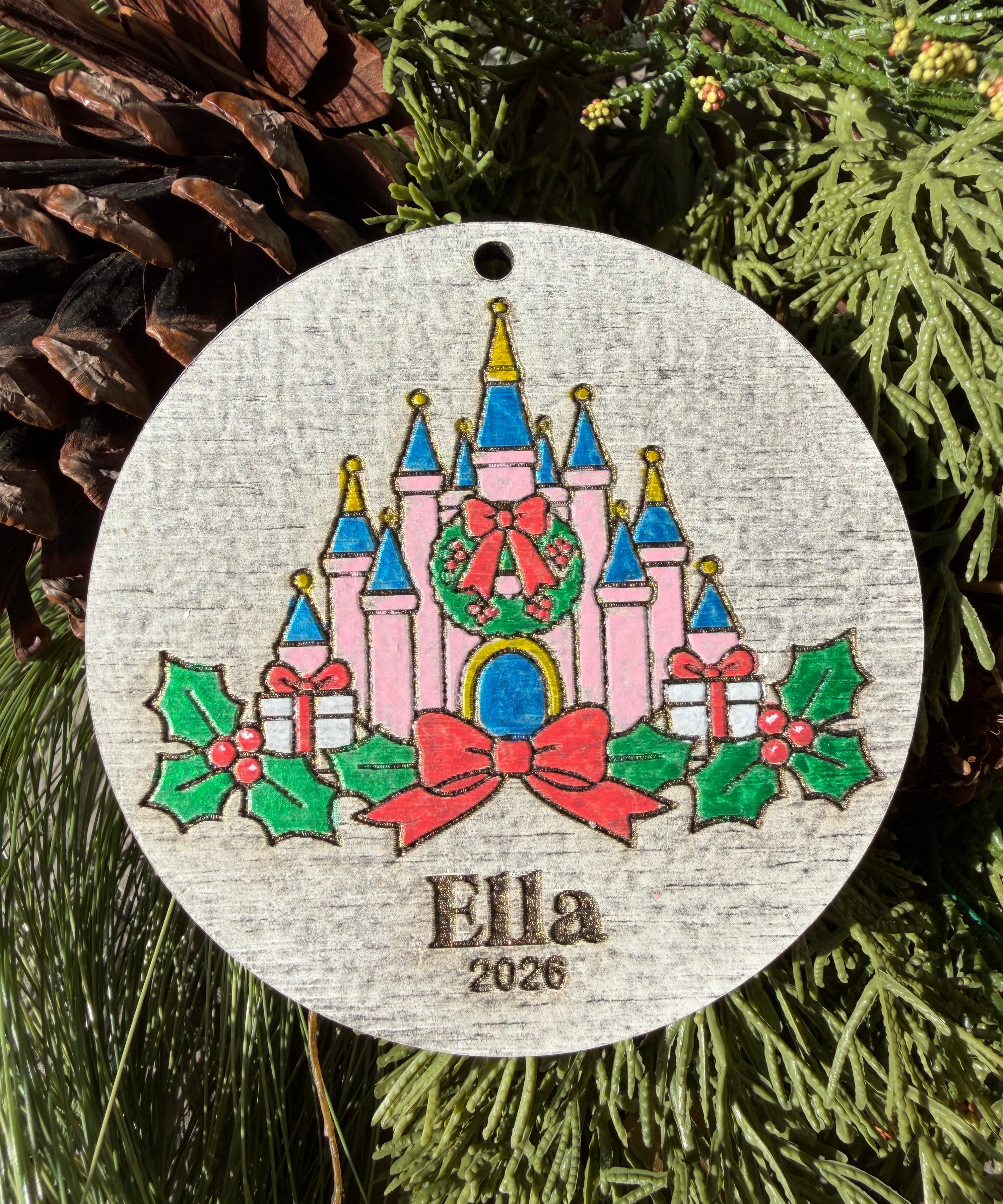 Finished hand-painted Holiday Storybook Castle on evergreen greenery. Personal name and year shown are sample personalization.