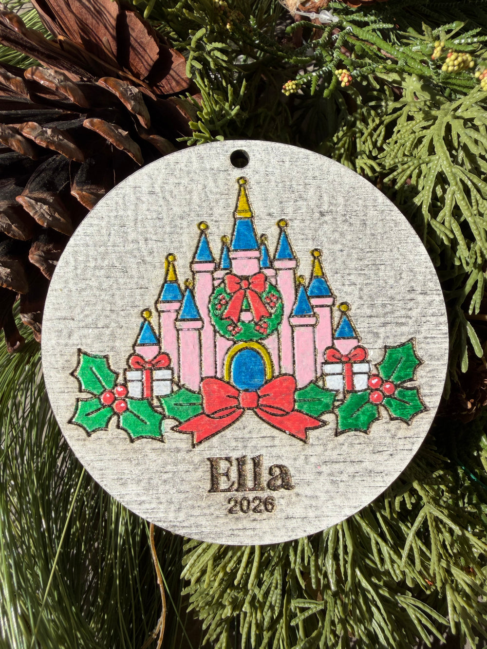 Finished hand-painted Holiday Storybook Castle on evergreen greenery. Personal name and year shown are sample personalization.