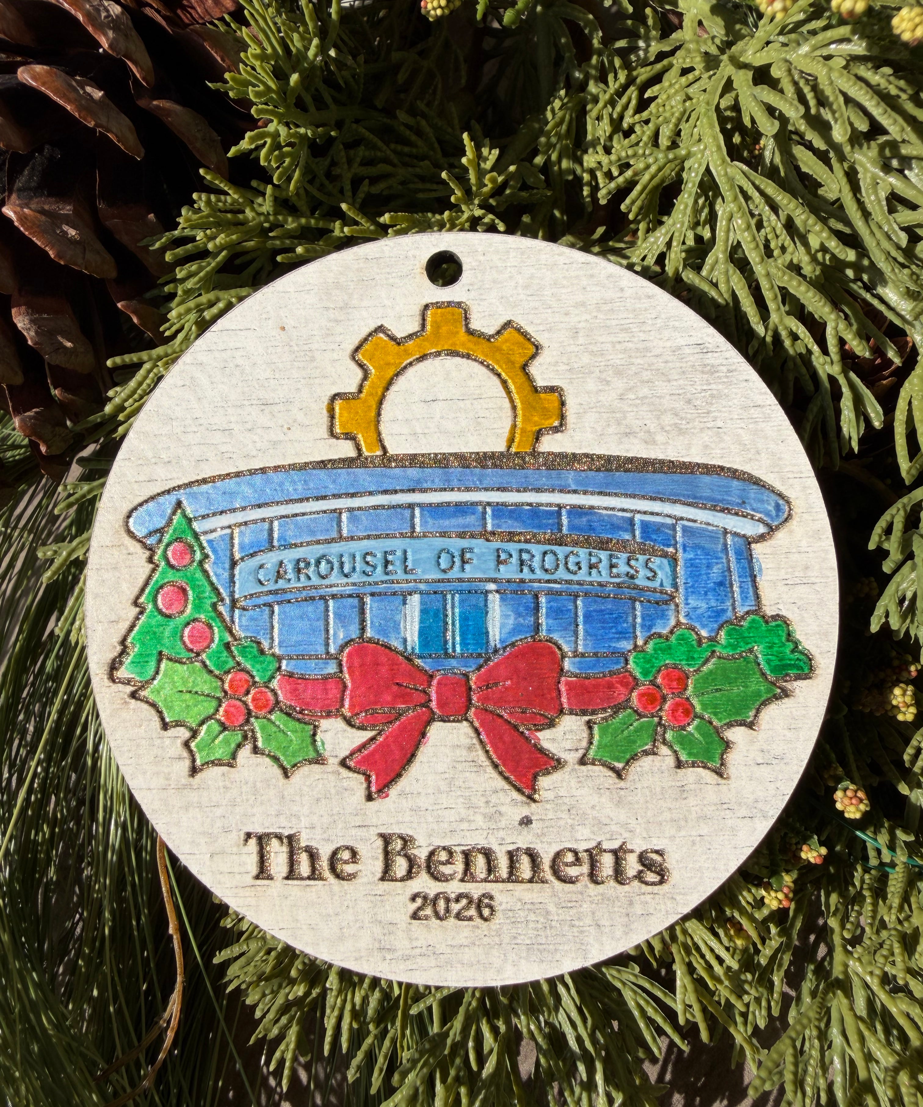 Finished hand-painted Carousel of Progress Christmas Ornament on evergreen greenery. Personal name and year shown are sample personalization.