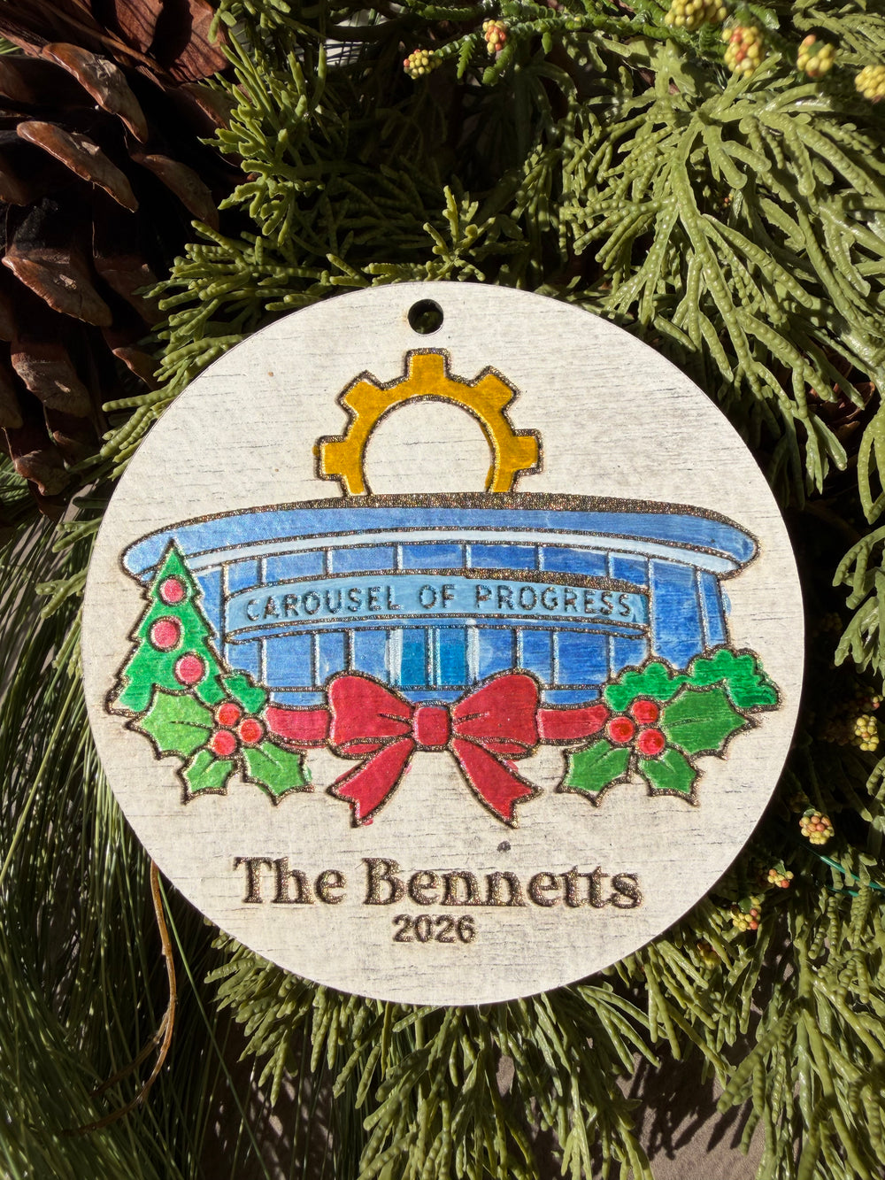 Finished hand-painted Carousel of Progress Christmas Ornament on evergreen greenery. Personal name and year shown are sample personalization.