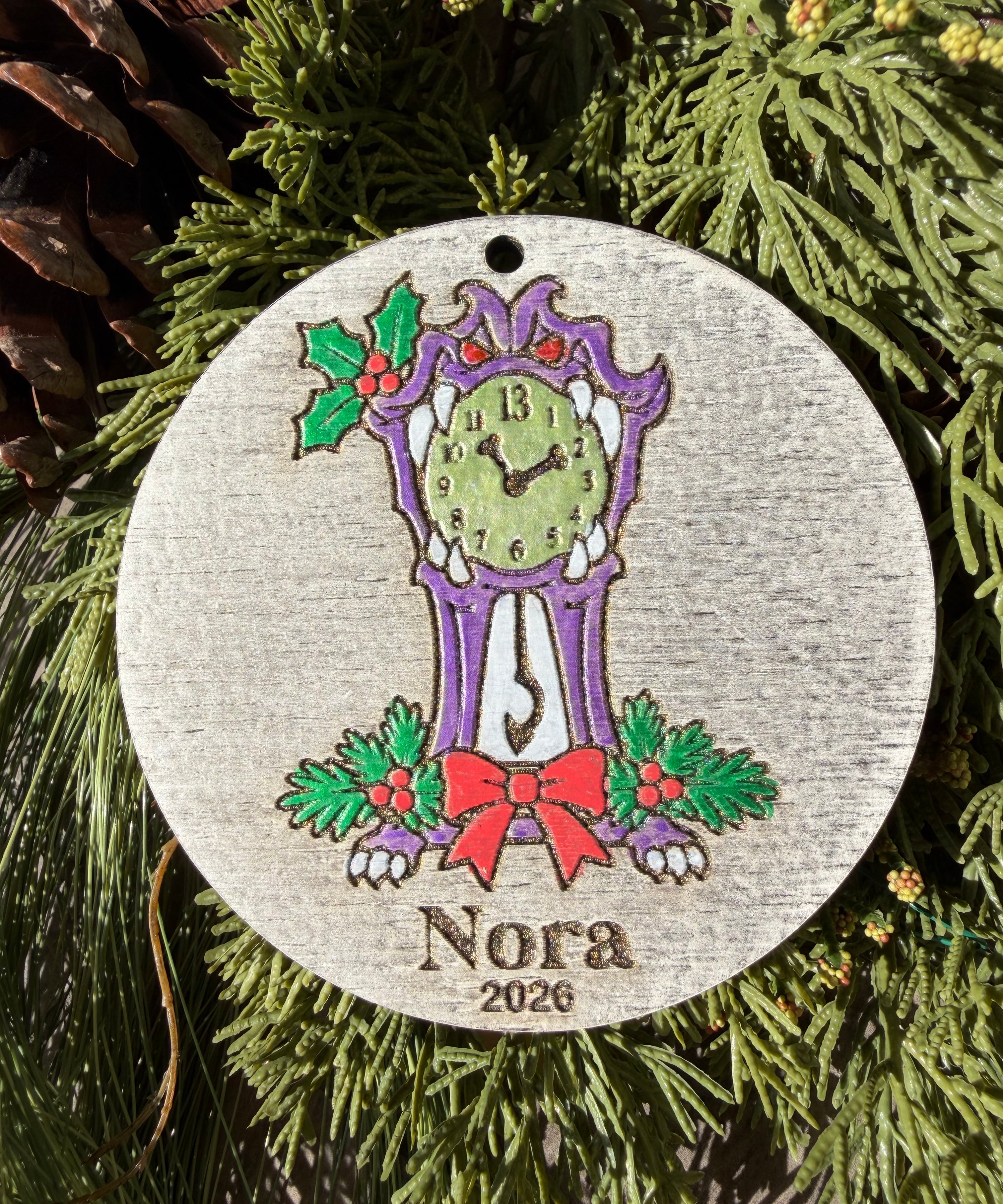 Finished hand-painted Haunted Mansion Clock Christmas Ornament on evergreen greenery. Personal name and year shown are sample personalization.