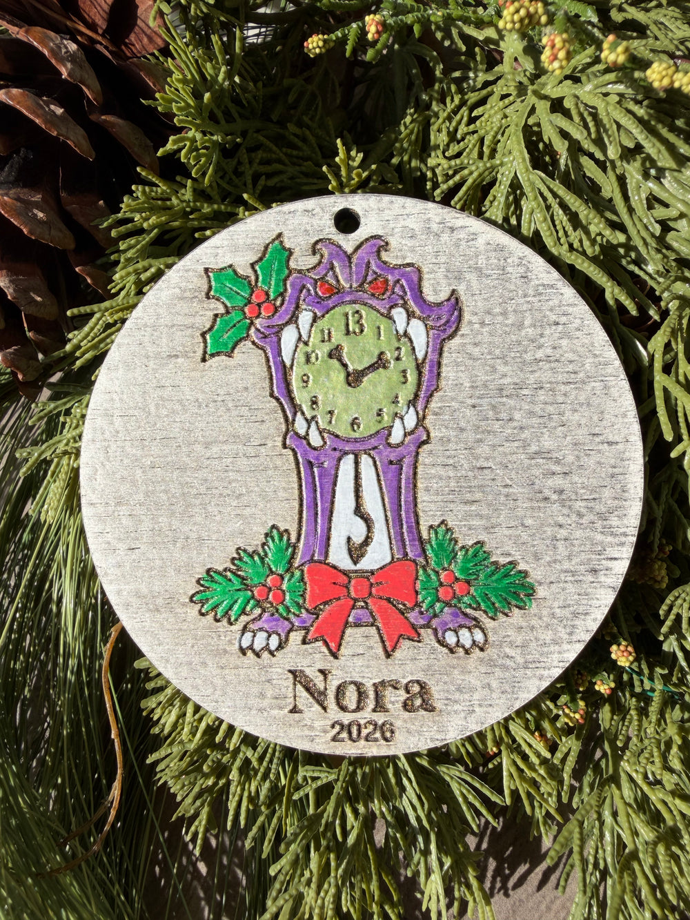 Finished hand-painted Haunted Mansion Clock Christmas Ornament on evergreen greenery. Personal name and year shown are sample personalization.