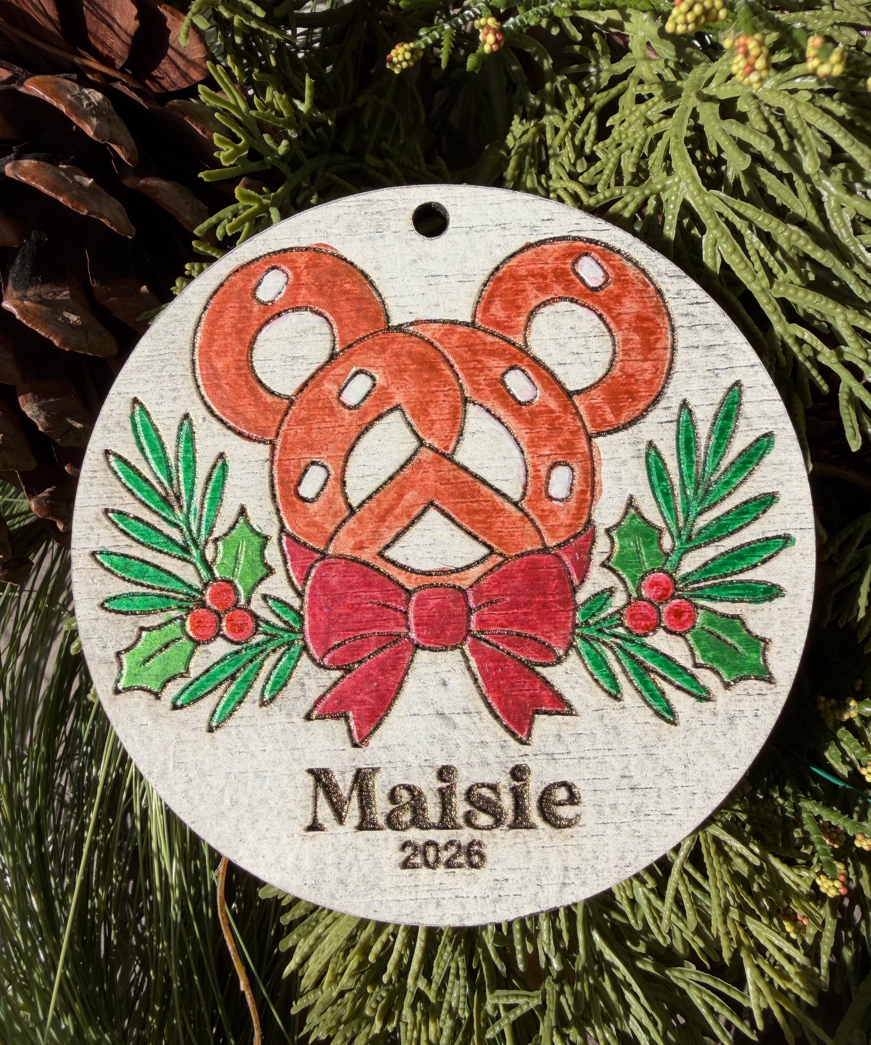 Finished hand-painted Park Pretzel Christmas Ornament on evergreen greenery. Personal name and year shown are sample personalization.