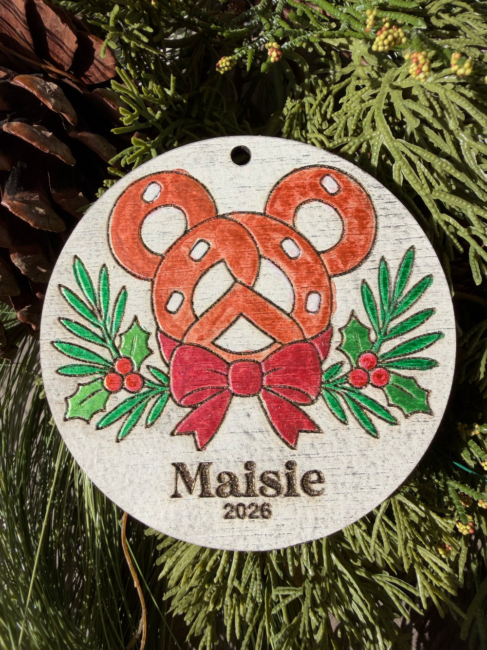 Finished hand-painted Park Pretzel Christmas Ornament on evergreen greenery. Personal name and year shown are sample personalization.