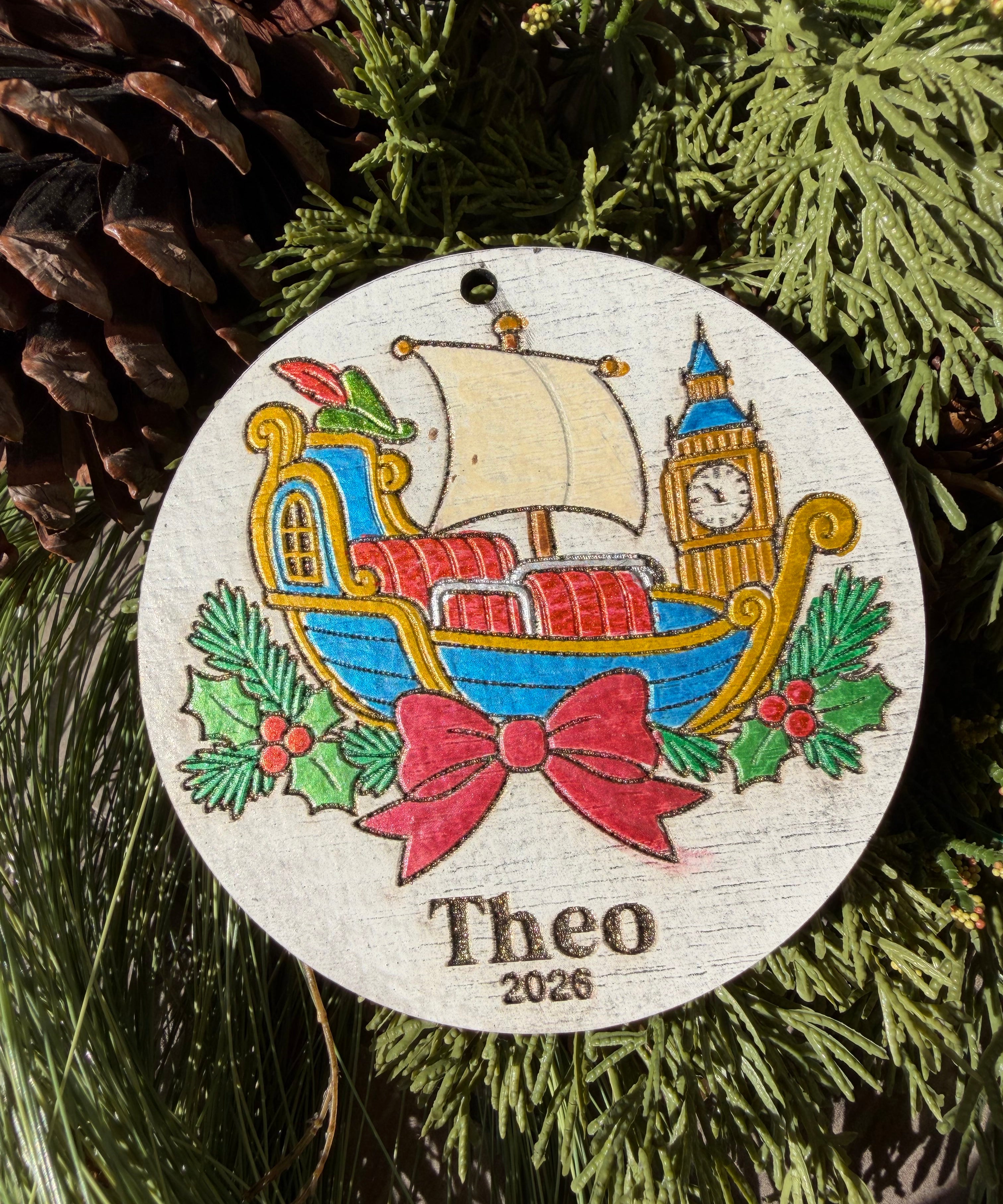 Finished hand-painted Neverland Flying Ship Christmas Ornament on evergreen greenery. Personal name and year shown are sample personalization.