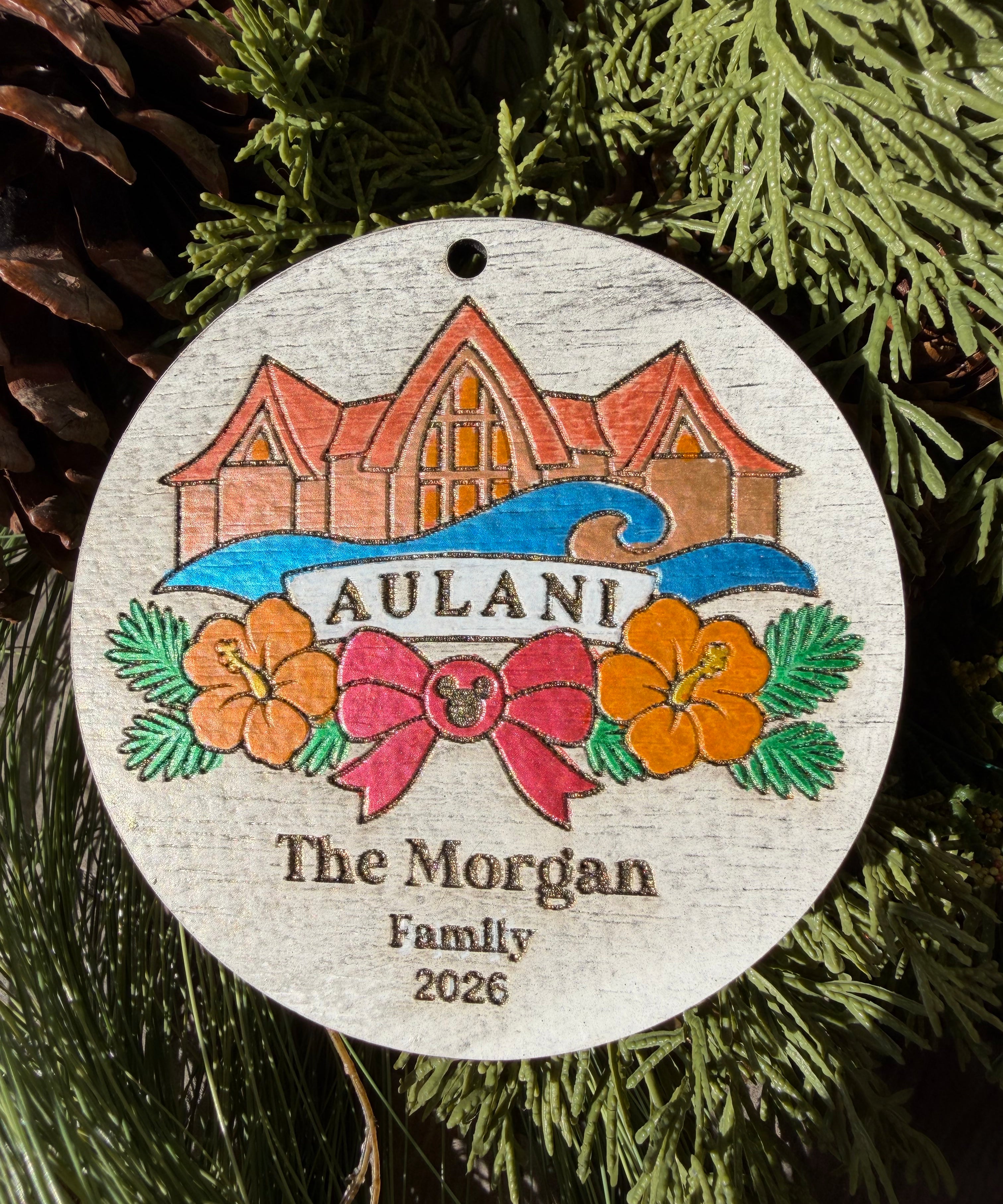 Finished hand-painted Aulani Christmas Ornament on evergreen greenery. Personal name and year shown are sample personalization.
