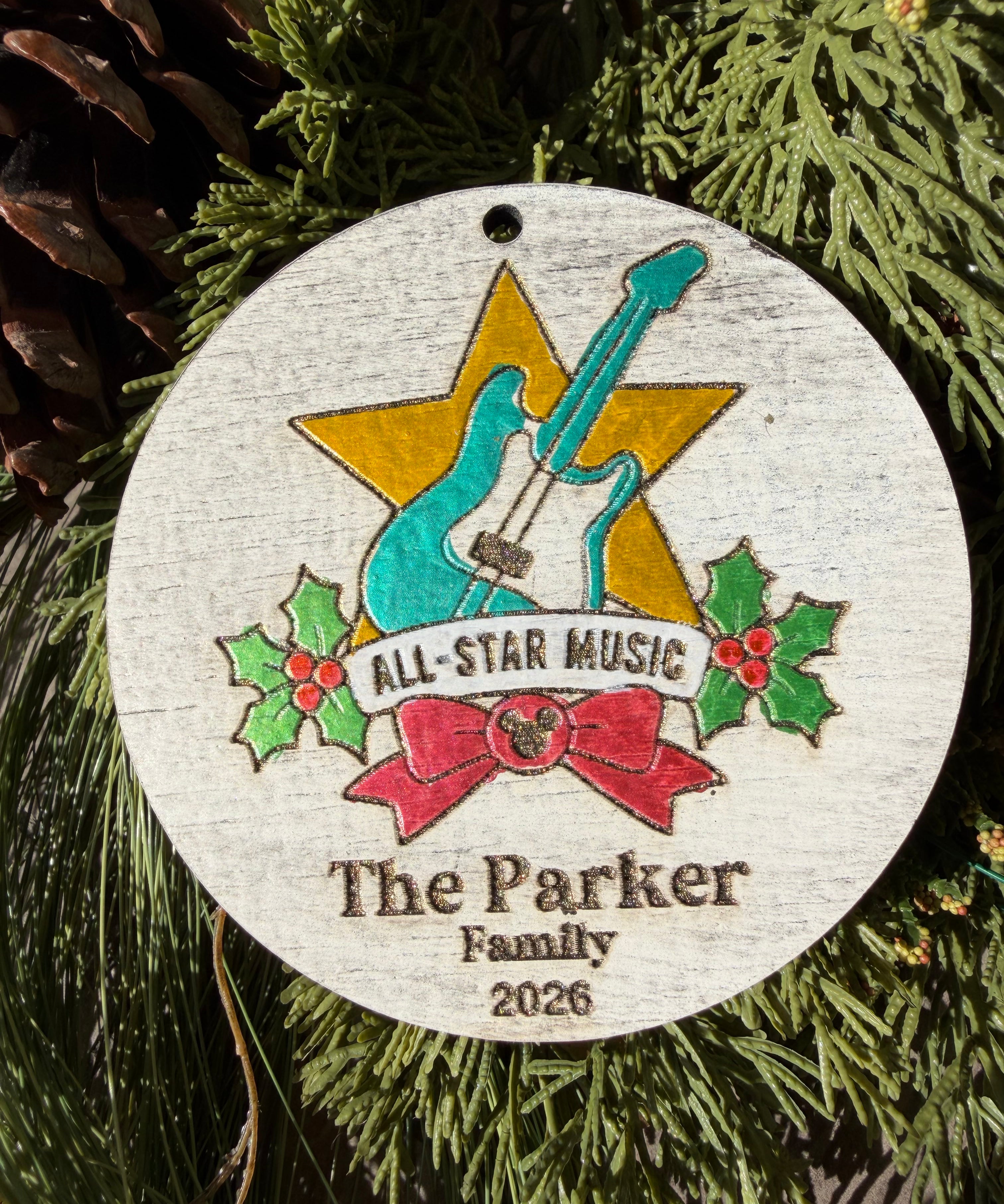 Finished hand-painted All-Star Music Christmas Ornament on evergreen greenery. Personal name and year shown are sample personalization.