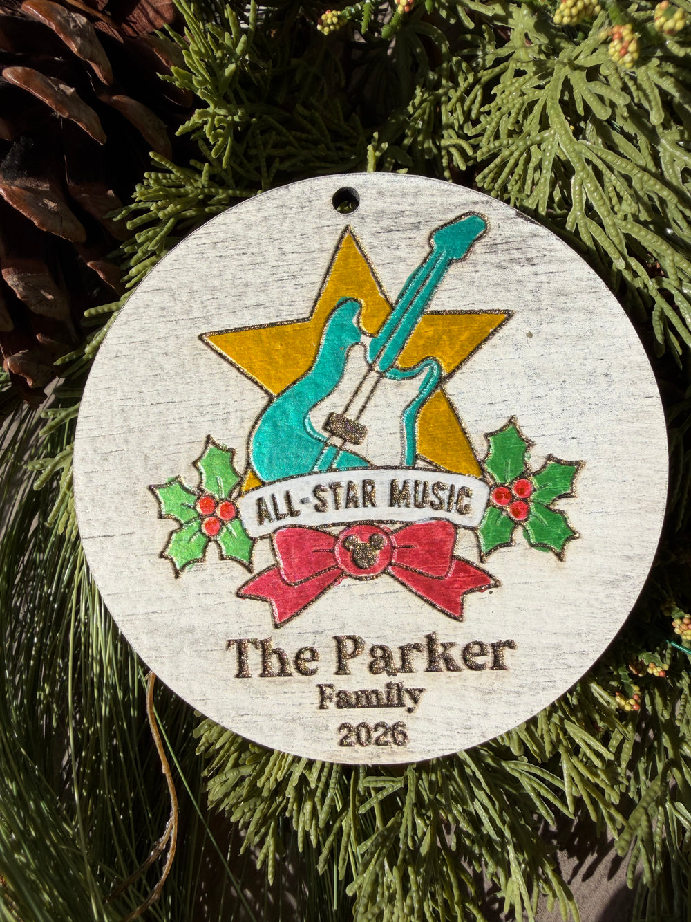 Finished hand-painted All-Star Music Christmas Ornament on evergreen greenery. Personal name and year shown are sample personalization.