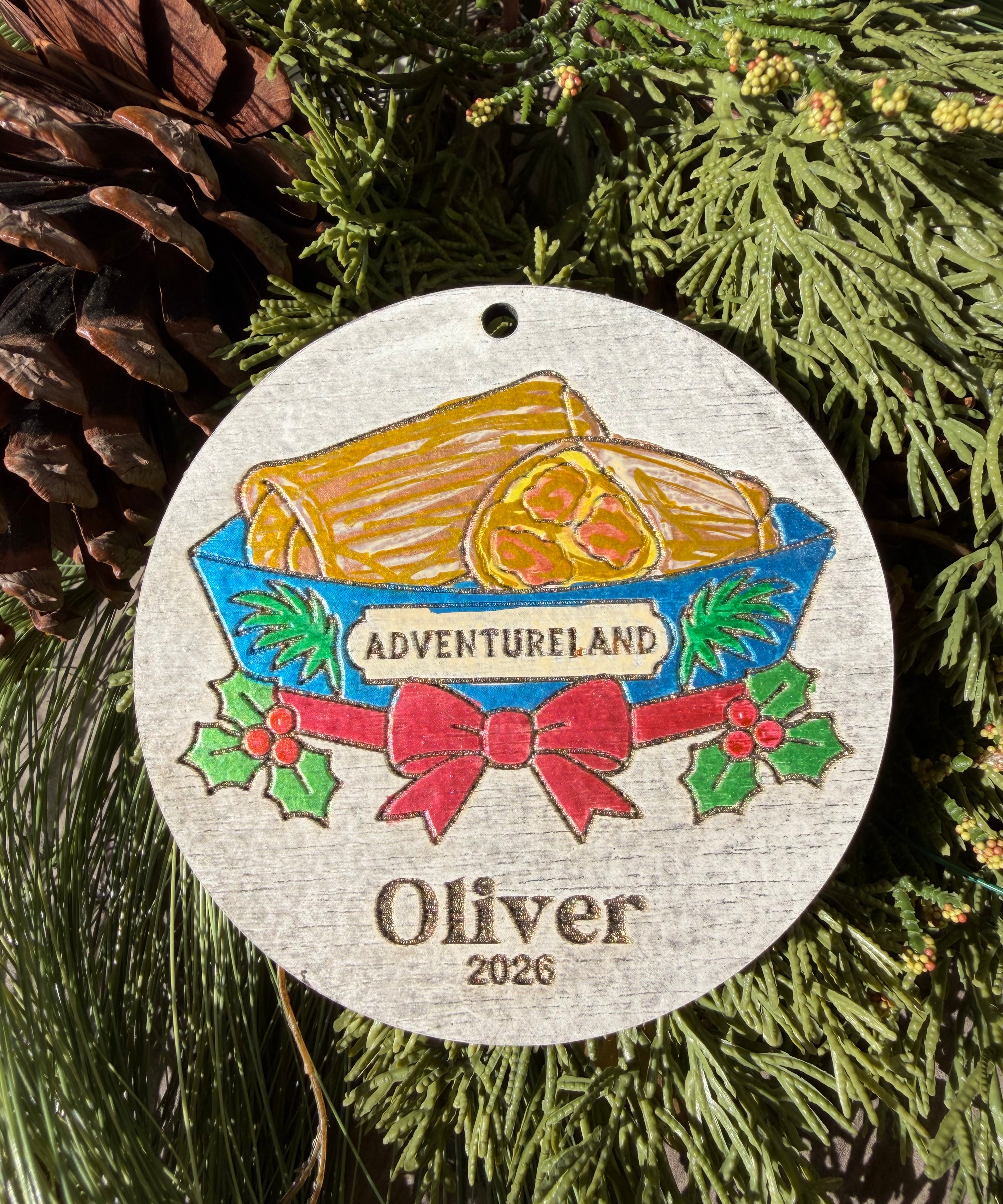 Finished hand-painted Adventureland Holiday Entrance on evergreen greenery. Personal name and year shown are sample personalization.