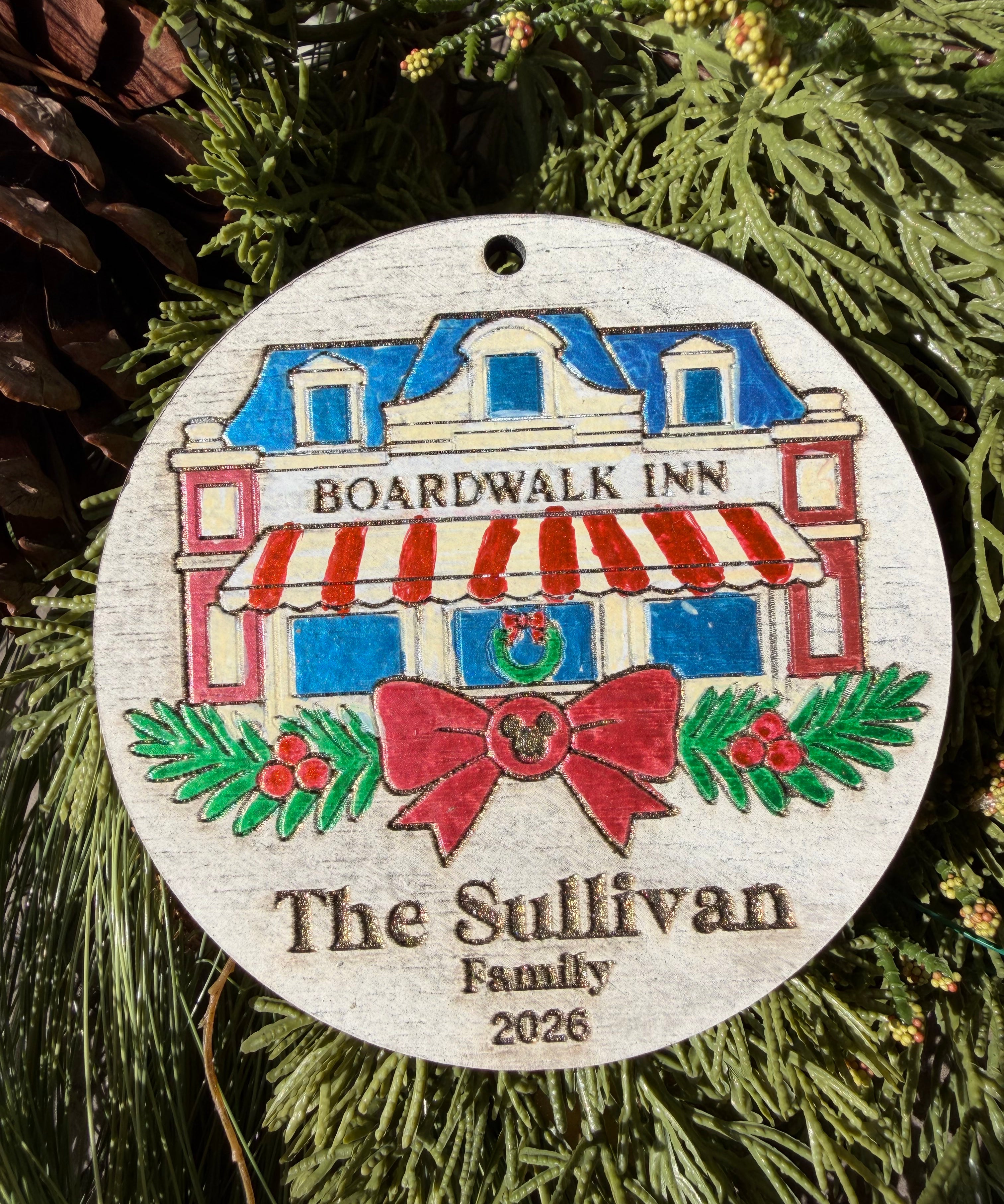 Finished hand-painted BoardWalk Inn Christmas Ornament on evergreen greenery. Personal name and year shown are sample personalization.