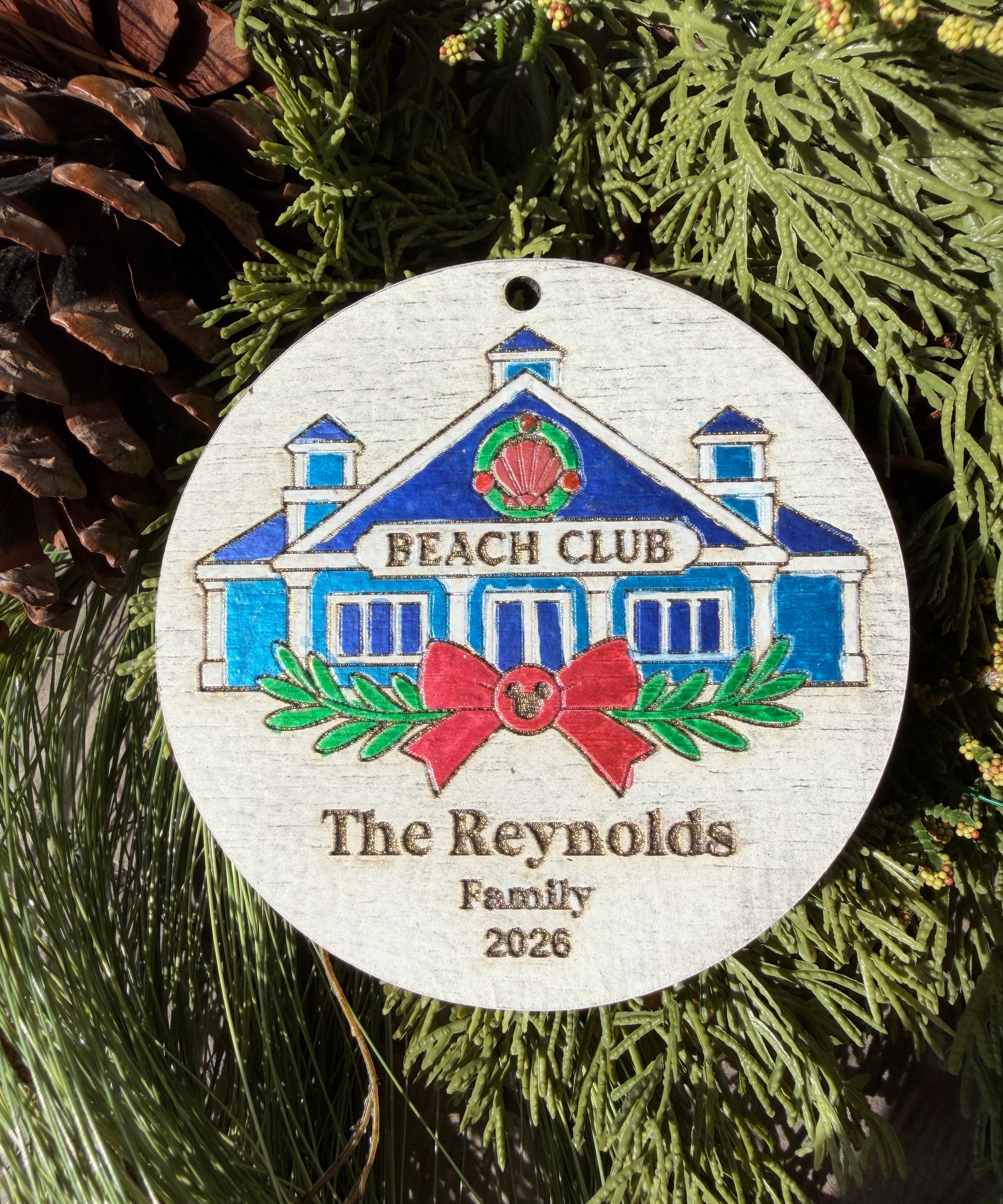 Finished hand-painted Beach Club Christmas Ornament on evergreen greenery. Personal name and year shown are sample personalization.