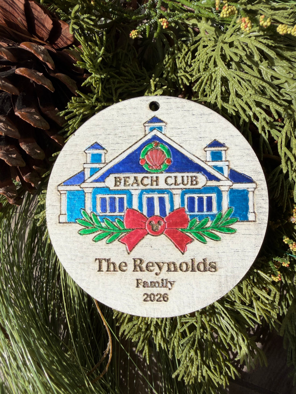 Finished hand-painted Beach Club Christmas Ornament on evergreen greenery. Personal name and year shown are sample personalization.
