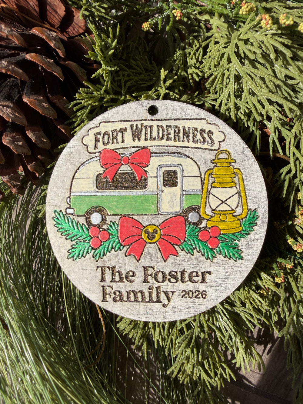Finished hand-painted Fort Wilderness Campsites Christmas Ornament on evergreen greenery. Personal name and year shown are sample personalization.