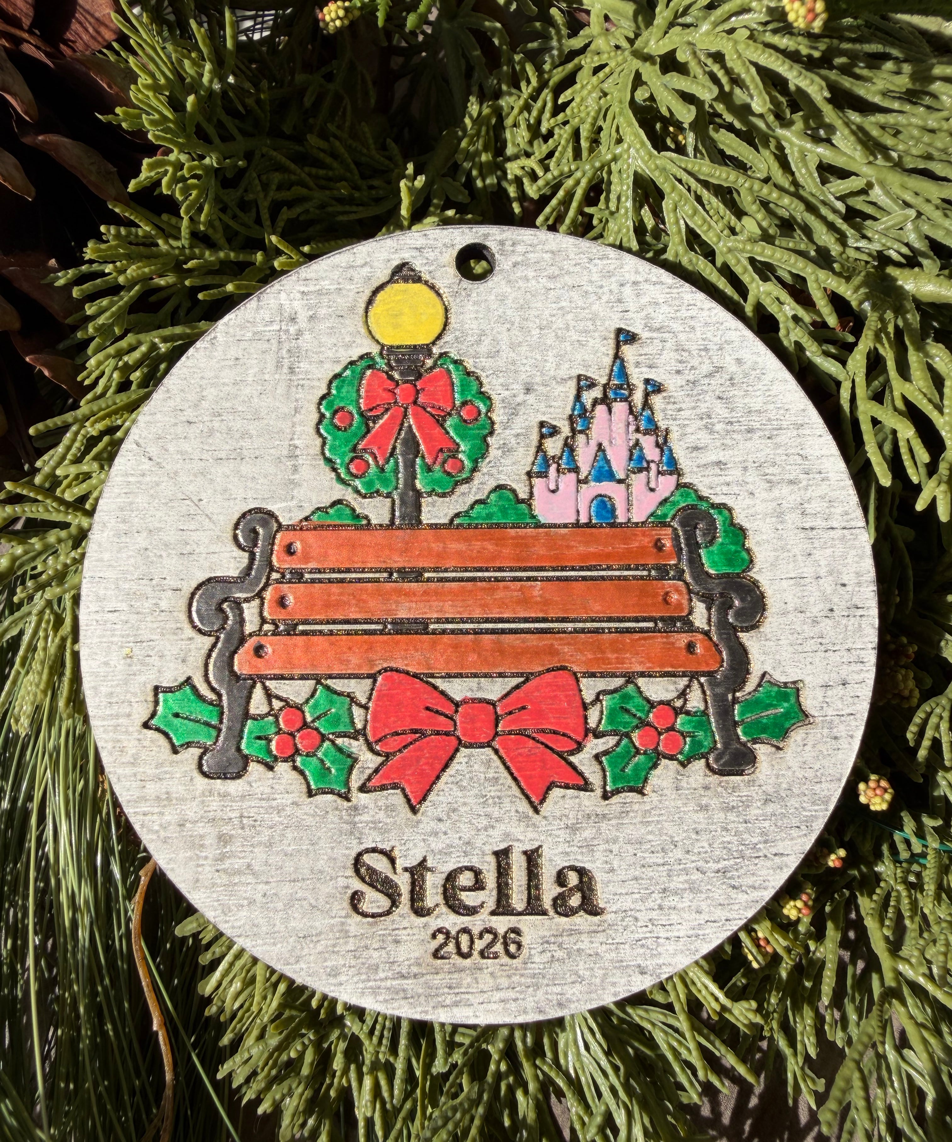 Finished hand-painted A Moment on Main Street Christmas Ornament on evergreen greenery. Personal name and year shown are sample personalization.