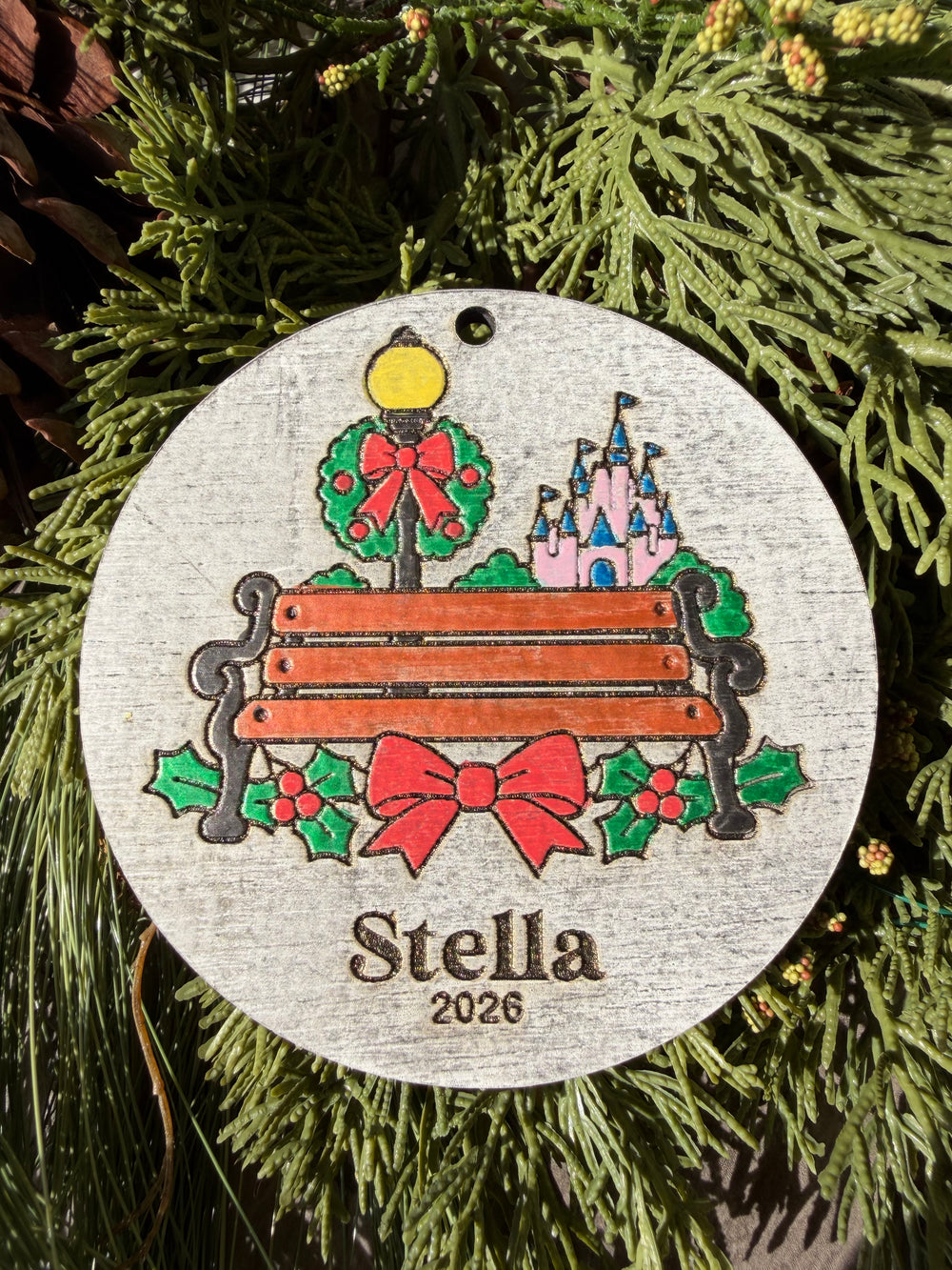 Finished hand-painted A Moment on Main Street Christmas Ornament on evergreen greenery. Personal name and year shown are sample personalization.