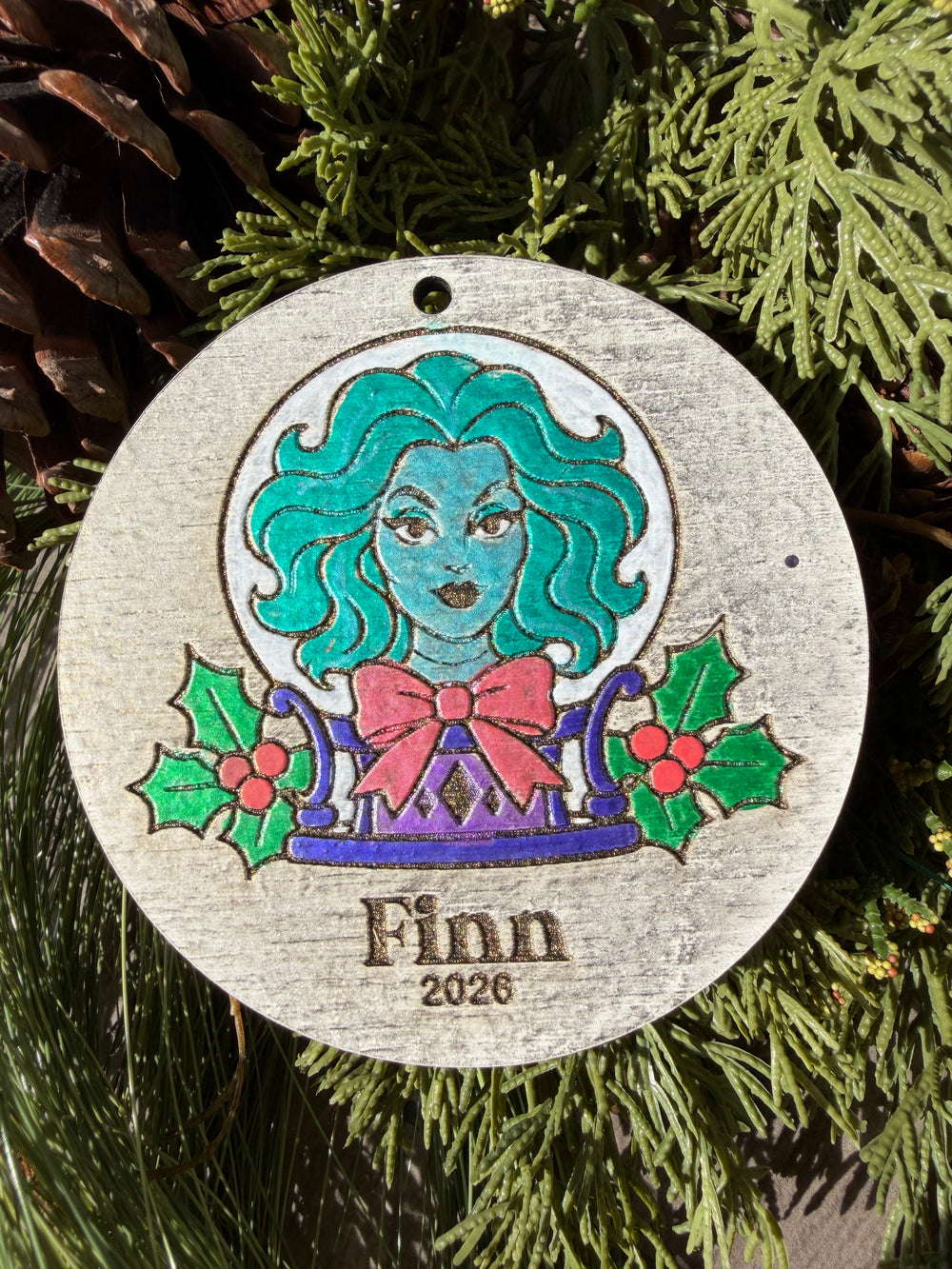 Finished hand-painted Madame Leota’s Christmas Ornament on evergreen greenery. Personal name and year shown are sample personalization.