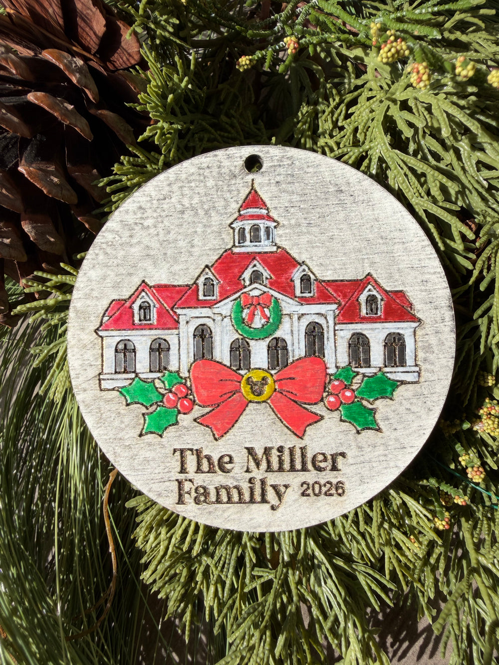 Finished hand-painted Grand Floridian Christmas Ornament on evergreen greenery. Personal name and year shown are sample personalization.
