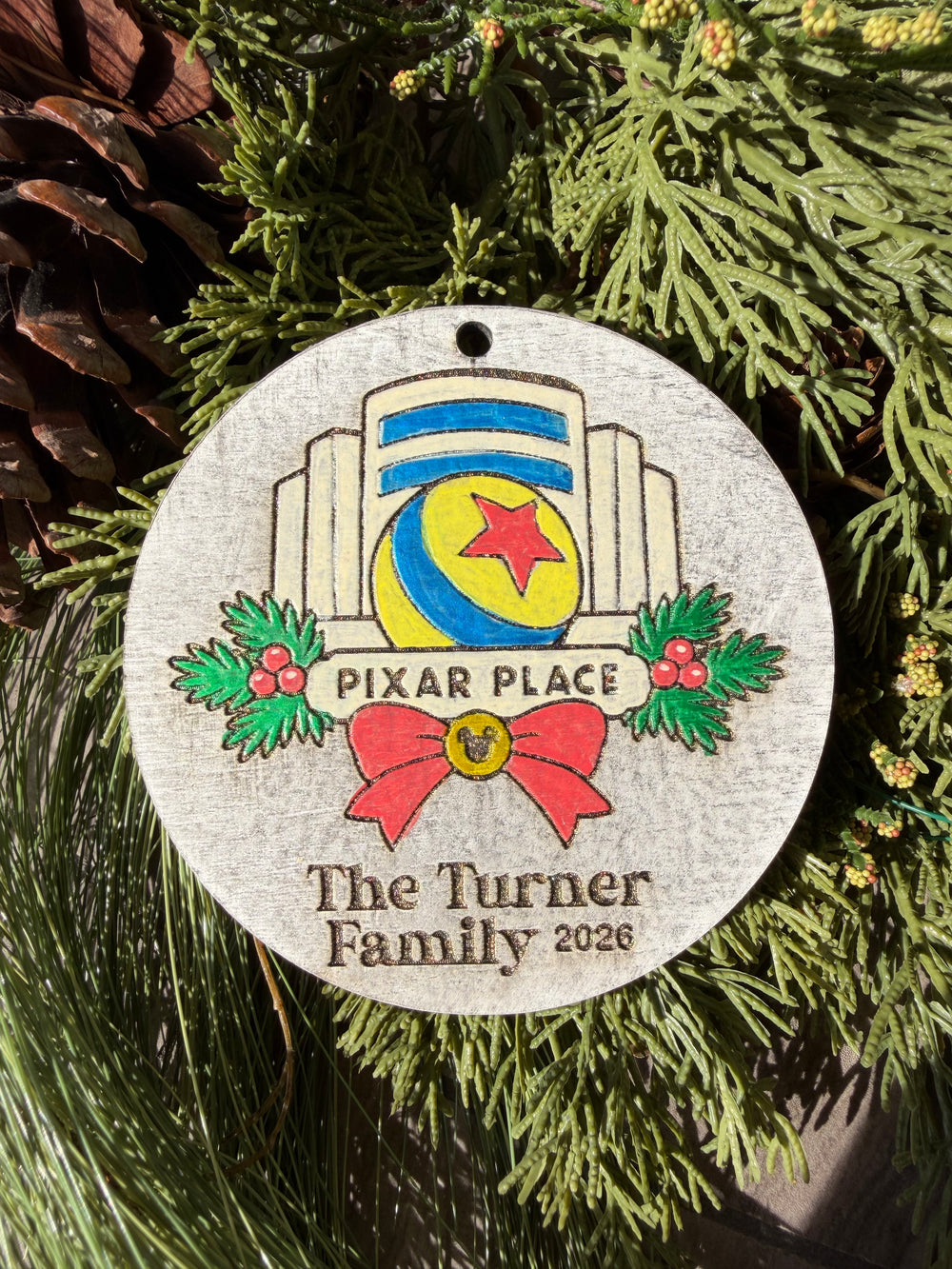 Finished hand-painted Animation Hotel Christmas Ornament on evergreen greenery. Personal name and year shown are sample personalization.