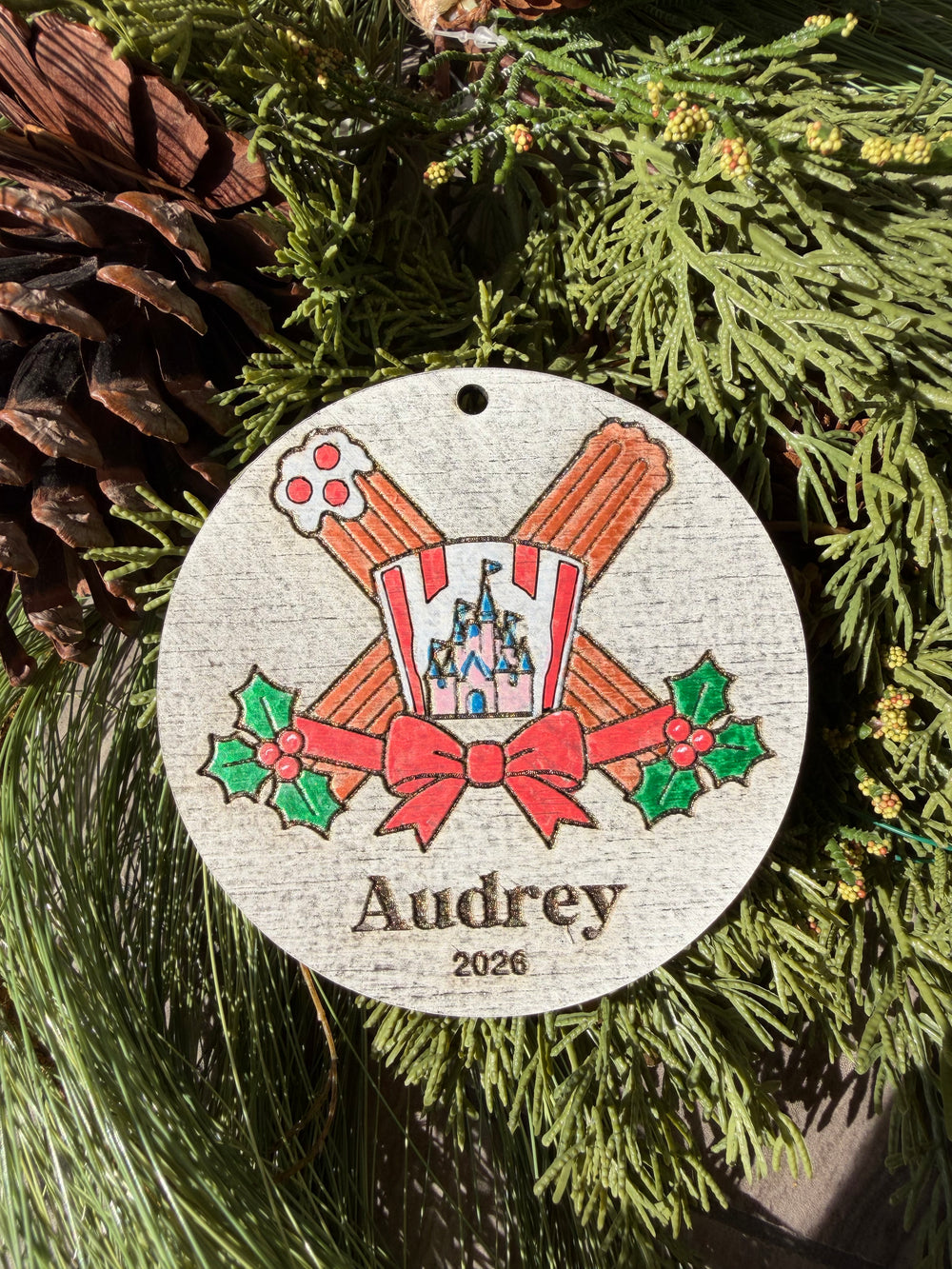 Finished hand-painted Holiday Churros Christmas Ornament on evergreen greenery. Personal name and year shown are sample personalization.