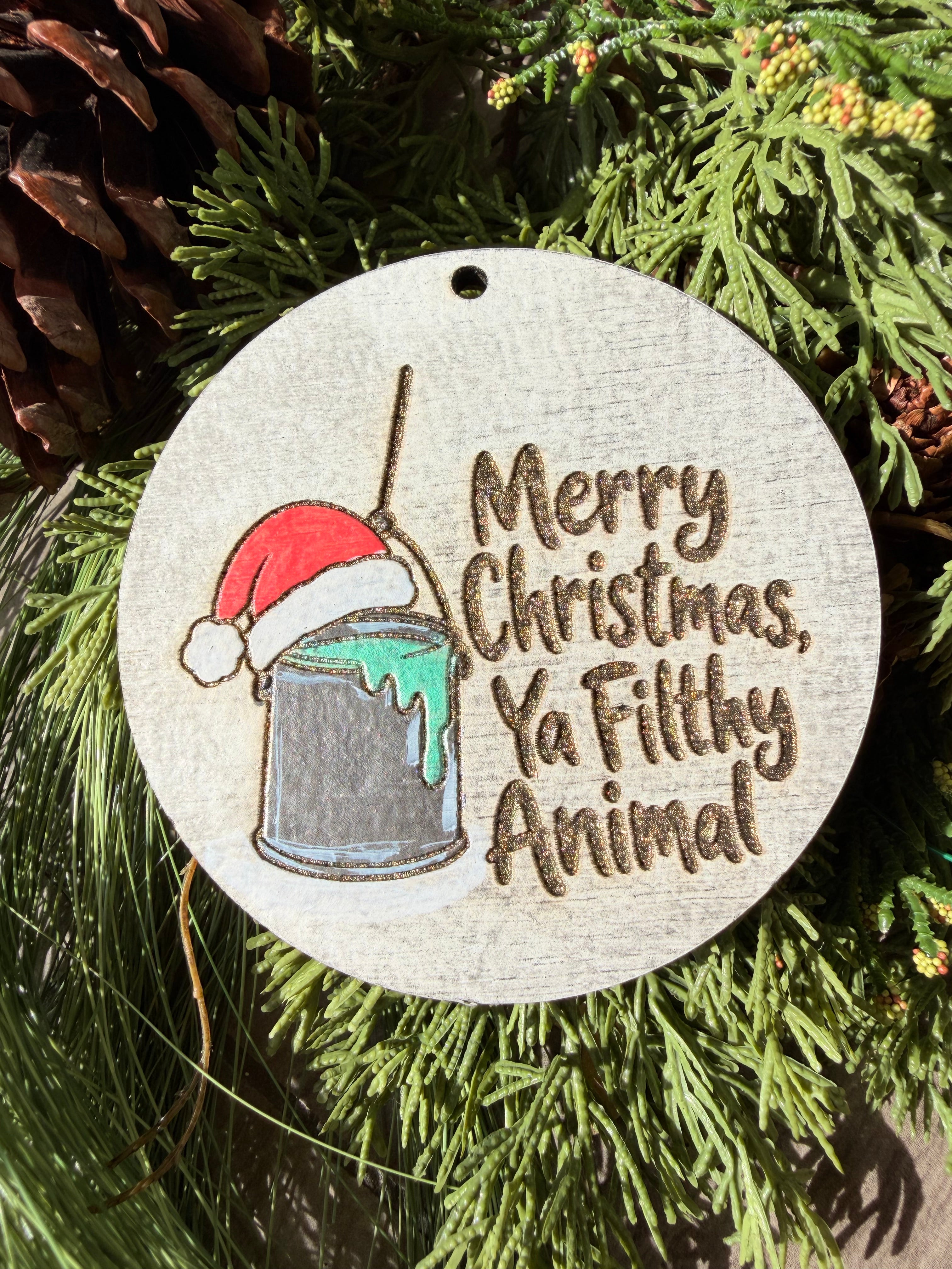 Finished hand-painted Merry Christmas, Ya Filthy Animal on evergreen greenery.
