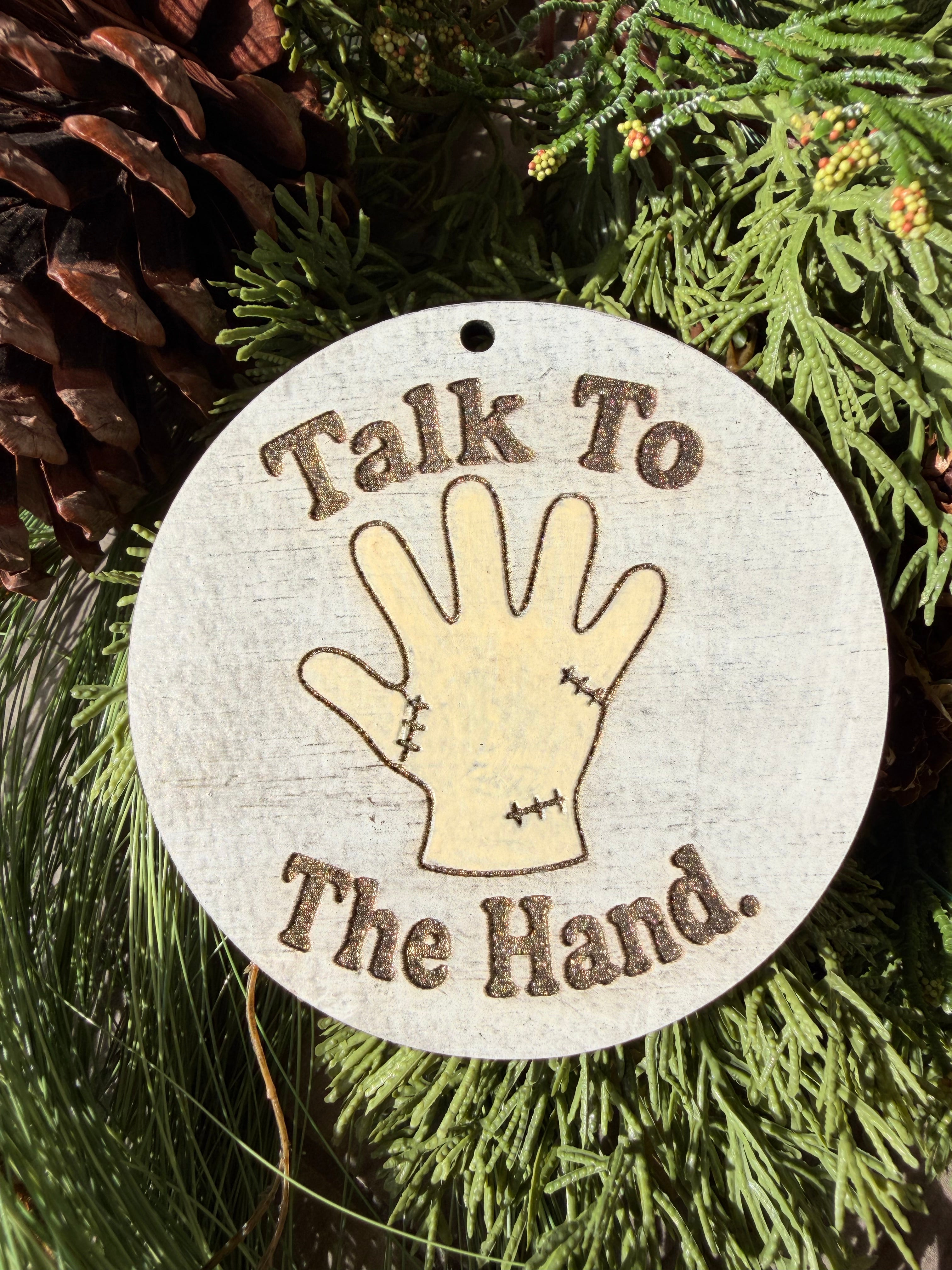 Finished hand-painted Talk to the Hand on evergreen greenery.