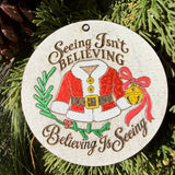 Finished hand-painted Seeing Isn’t Believing on evergreen greenery.