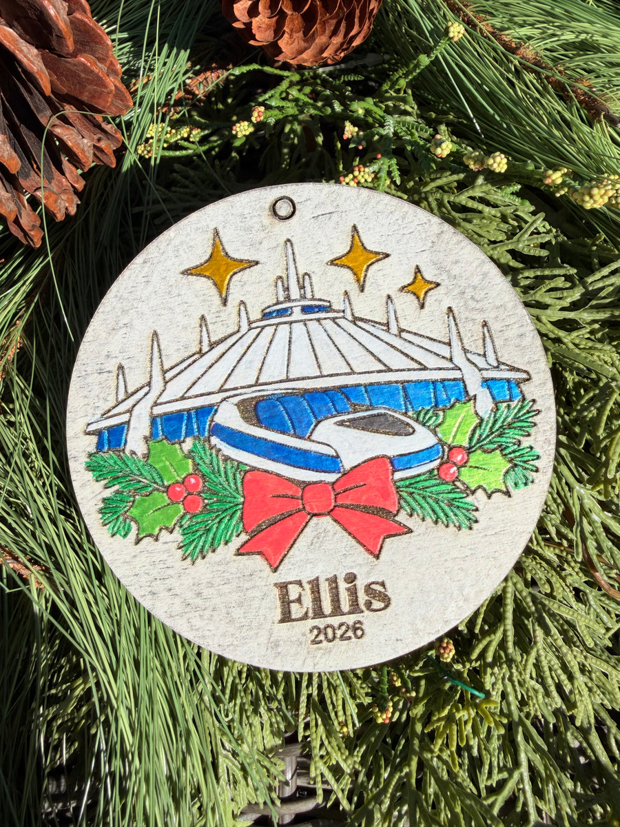 Finished hand-painted Space Mountain Christmas Ornament on evergreen greenery. Name and year shown are sample personalization.