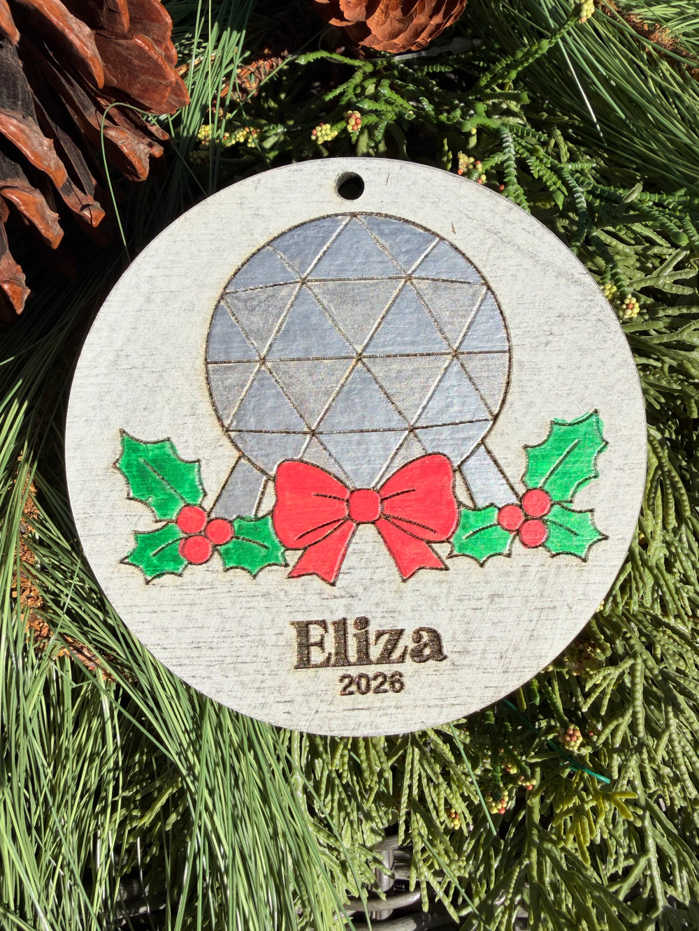 Finished hand-painted Spaceship Earth Christmas Ornament on evergreen greenery. Name and year shown are sample personalization.