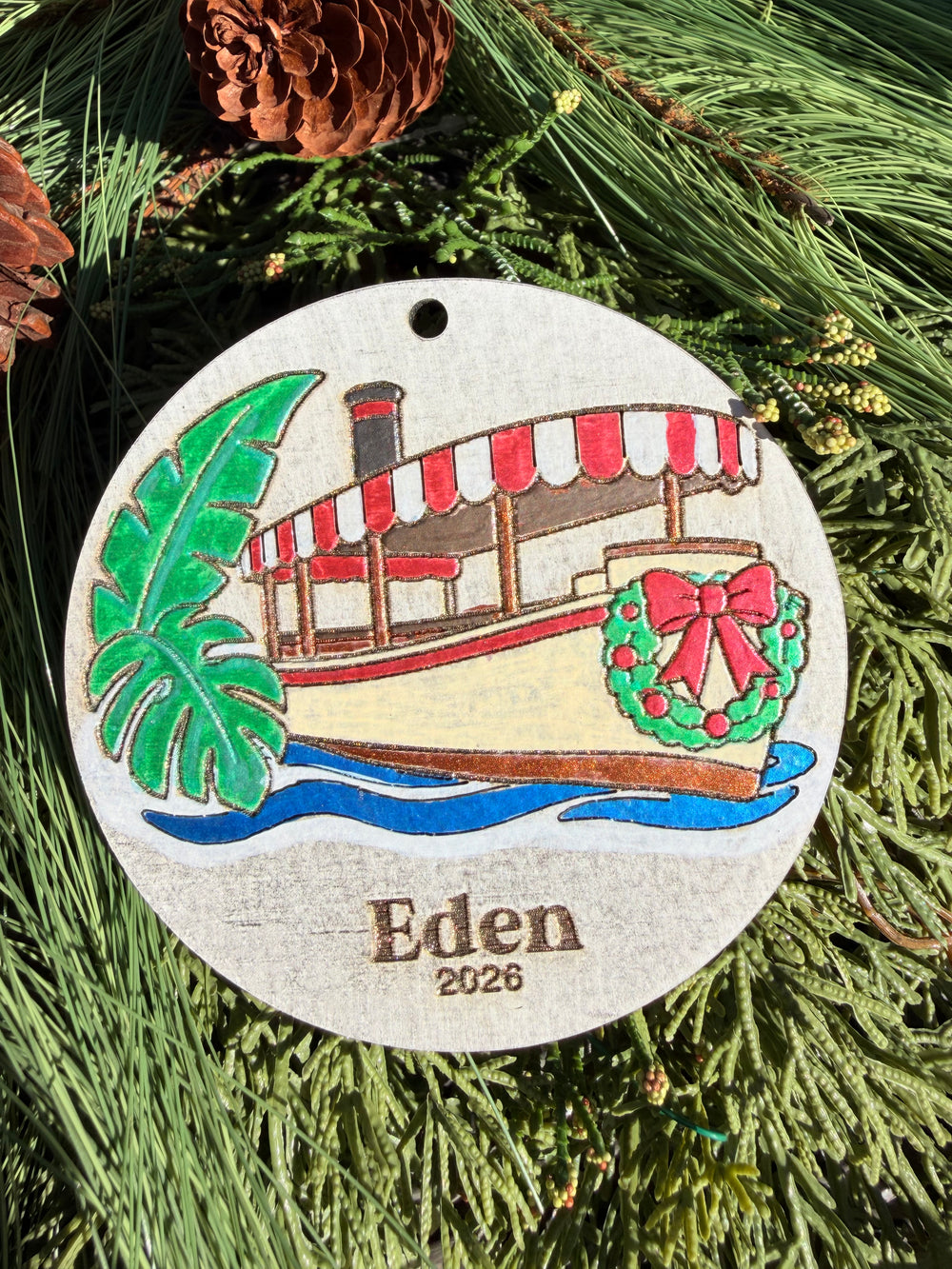 Finished hand-painted Jungle Cruise Christmas Ornament on evergreen greenery. Name and year shown are sample personalization.