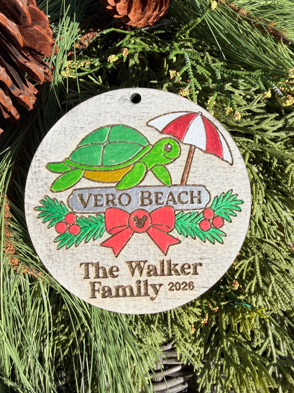Finished hand-painted Vero Beach Christmas Ornament on evergreen greenery. Name and year shown are sample personalization.